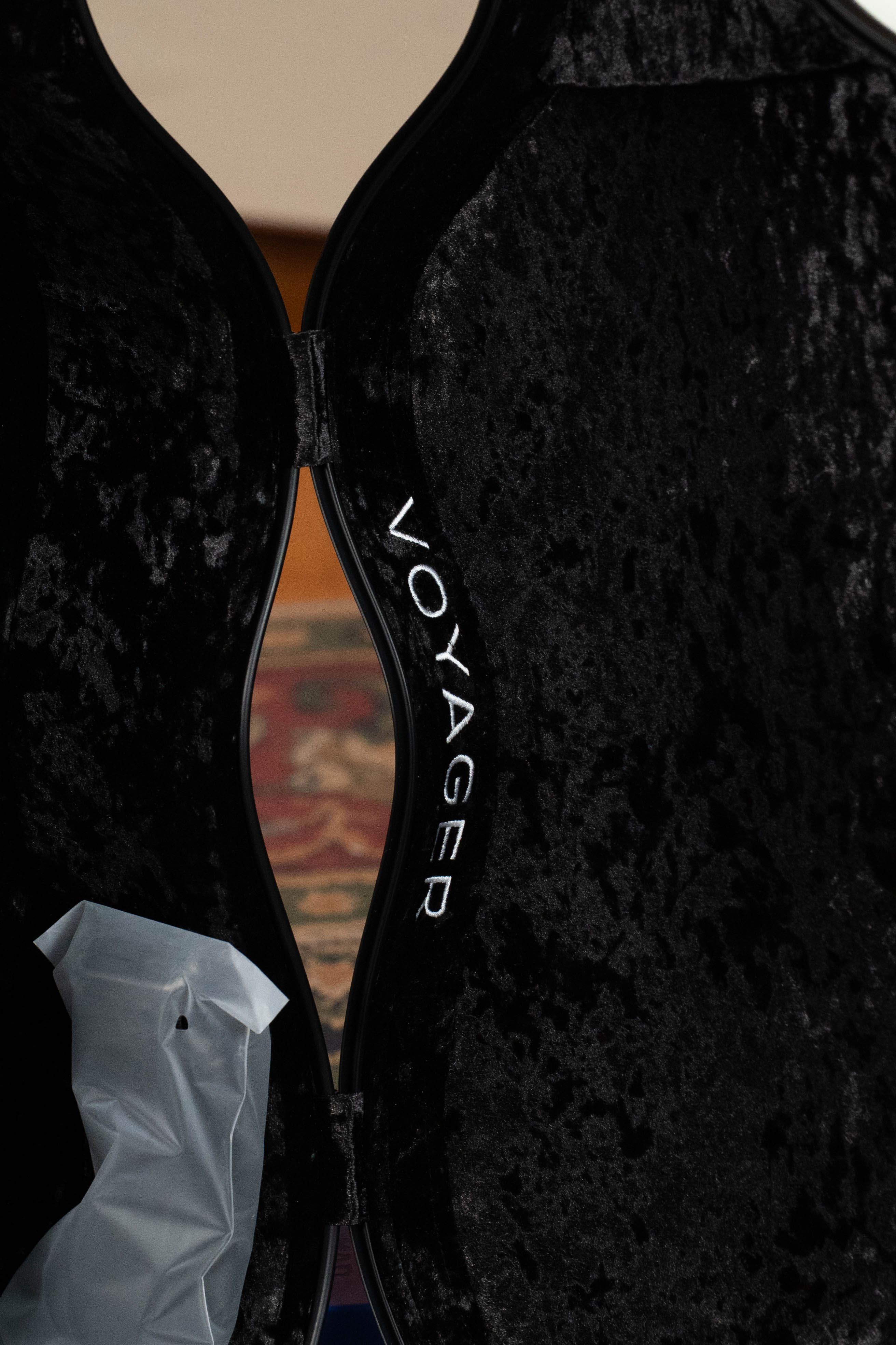 A lightweight TKL Voyager Universal Pearl Glacier/Blue Carbon Fiber Dreadnought case, open to reveal a black velvet interior with "VOYAGER" embroidered in white. A translucent plastic piece and a patterned rug are also visible.