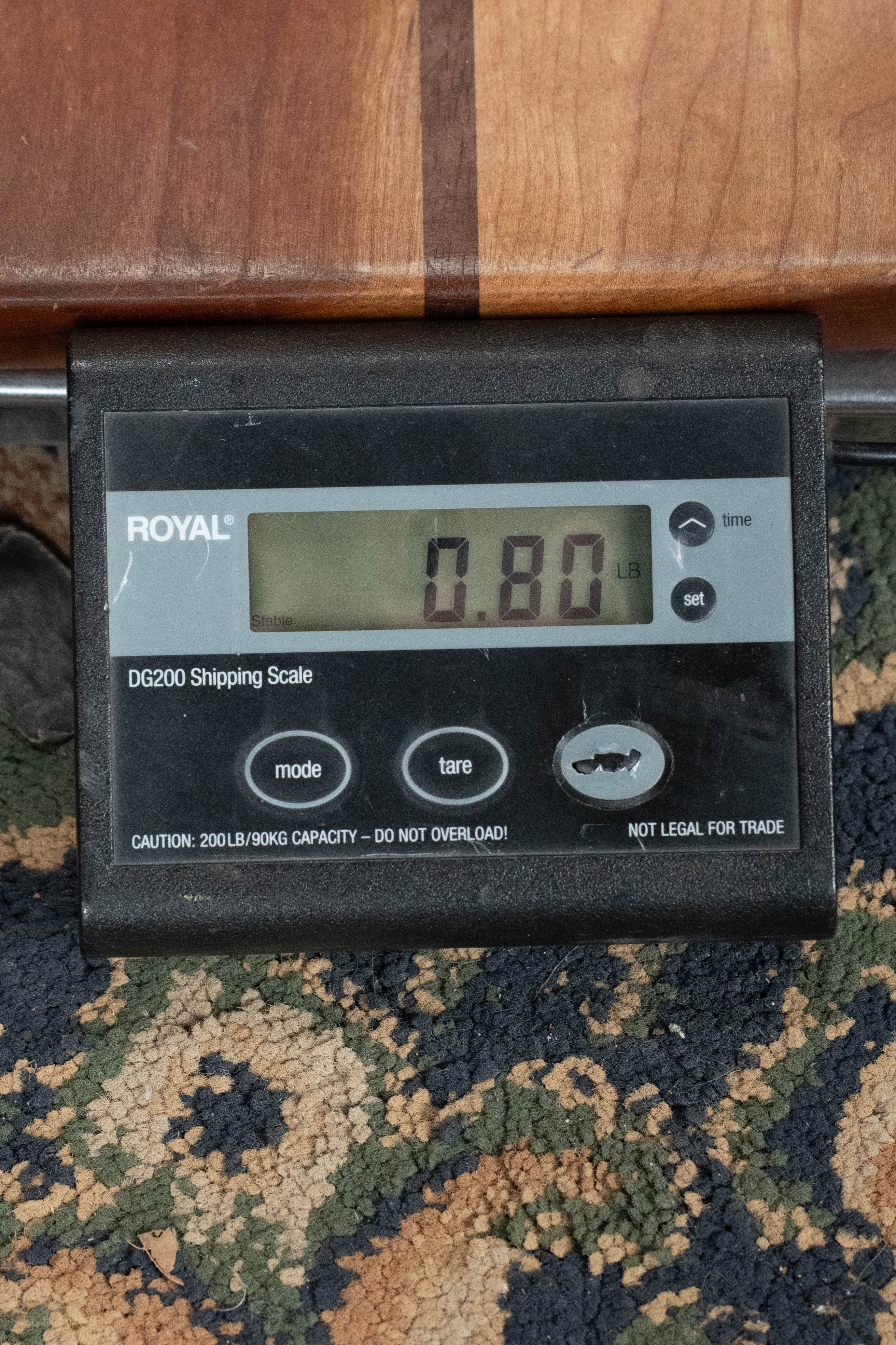 Digital scale displaying 0.80 pounds with ukulele body edge visible above on patterned carpet. - The Waterman Aqua Mist Glow-In-The-Dark Soprano Recycled Ukulele - Kala Brand - Default Title