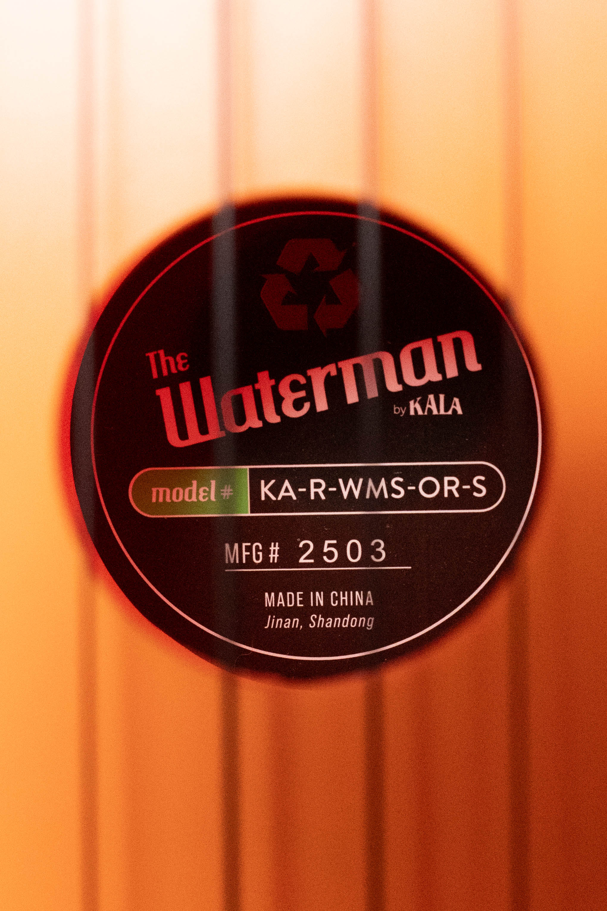 Close-up of Waterman Sunset Orange soprano ukulele soundhole label showing model and serial number. - The Waterman Sunset Orange Soprano Recycled Ukulele - Kala Brand - Default Title