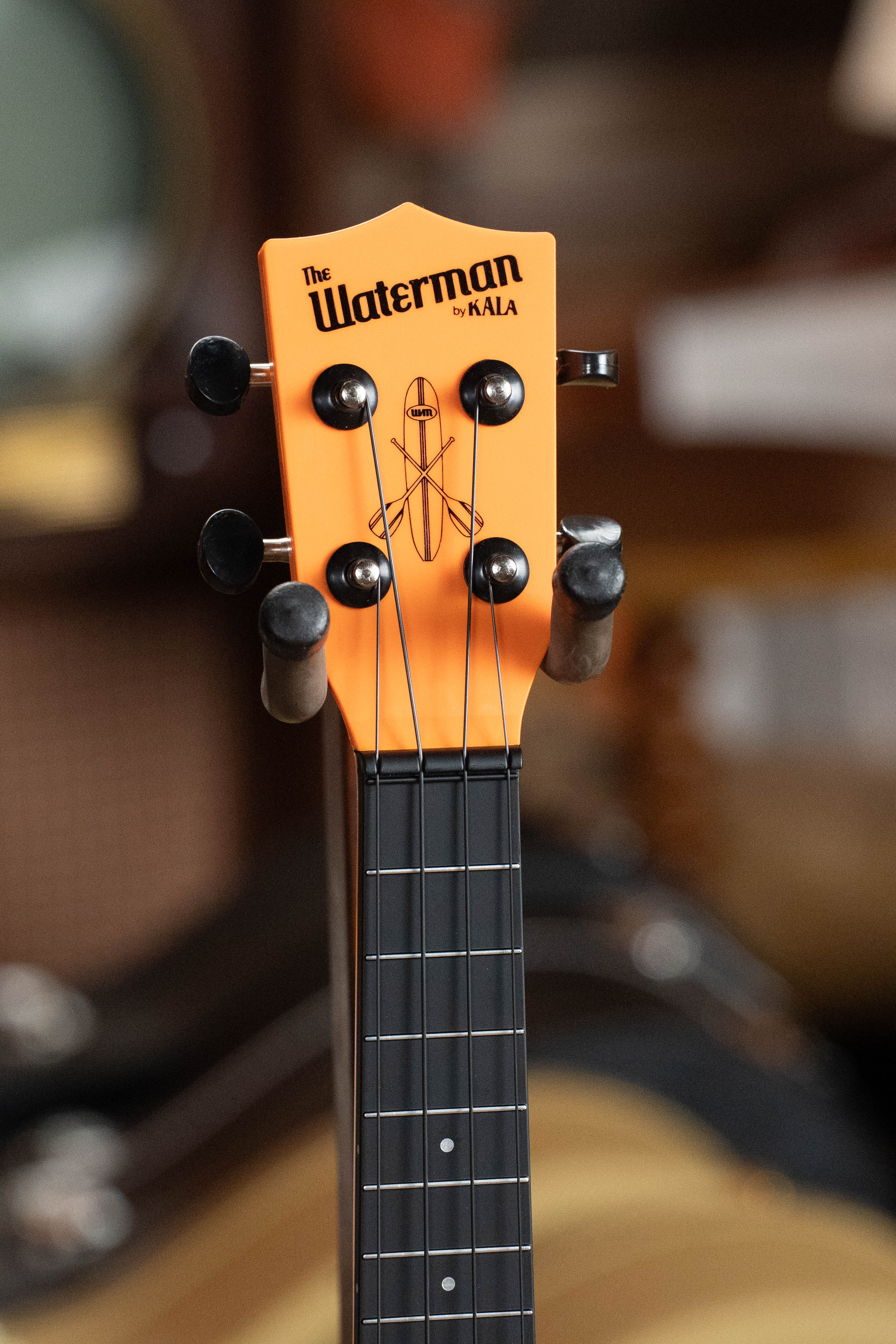 Kala Waterman Sunset Orange soprano ukulele headstock with black tuning pegs and logo against blurred background. - The Waterman Sunset Orange Soprano Recycled Ukulele - Kala Brand - Default Title