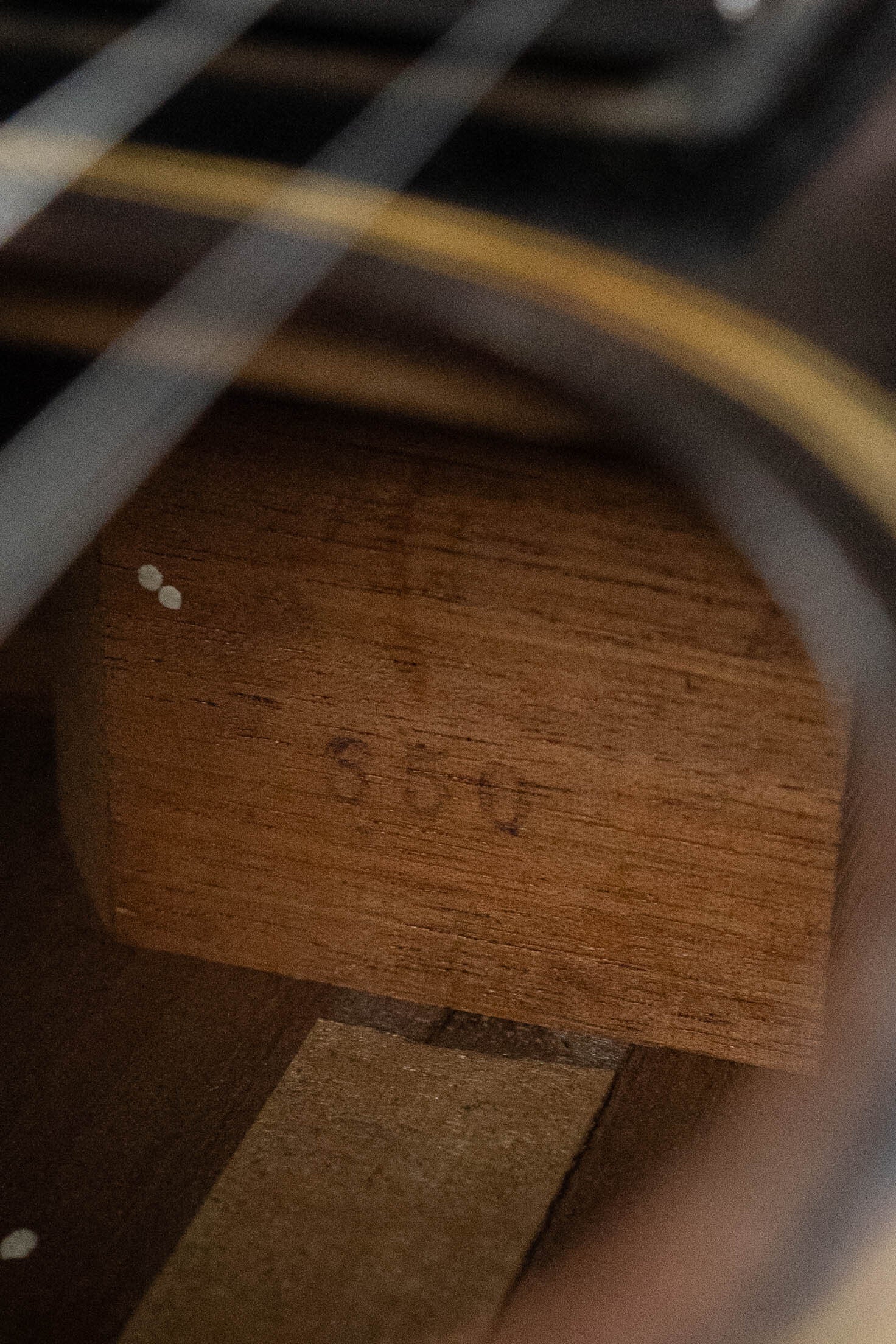 Close-up of the interior of a (Used) 1933 Gibson LOO Adirondack/Mahogany OO Tobacco Sunburst Acoustic Guitar #550 by Gibson, highlighting a wooden support block with faint handwritten numbers and visible strings above.