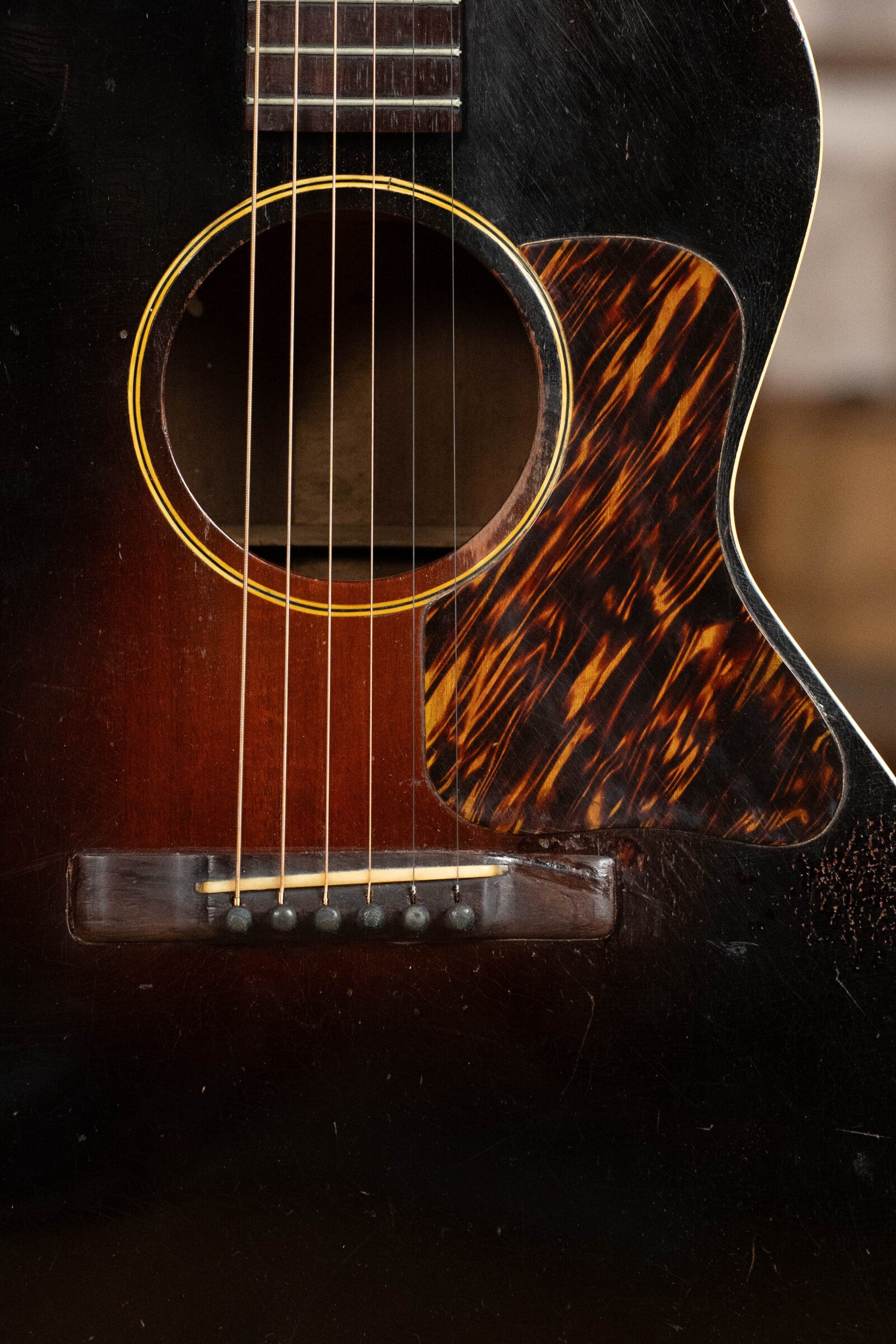Close-up of a (Used) 1933 Gibson LOO Adirondack/Mahogany OO Tobacco Sunburst Acoustic Guitar #550 by Gibson, featuring a yellow-ringed sound hole, tortoiseshell pickguard, six strings, and a dark mahogany body with visible scratches.