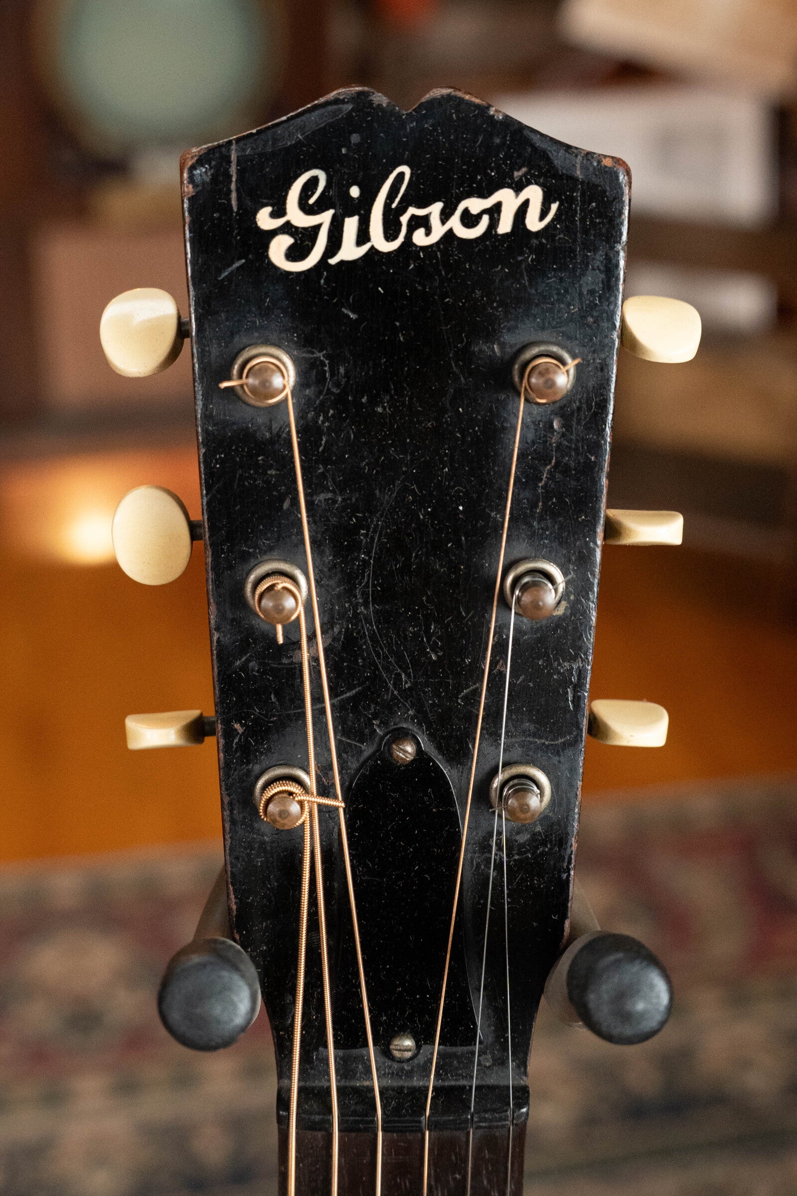 Close-up of a black Gibson headstock with vintage tuning pegs and strings from a (Used) 1933 Gibson LOO Adirondack/Mahogany OO Tobacco Sunburst Acoustic Guitar #550, photographed indoors against a blurred background.