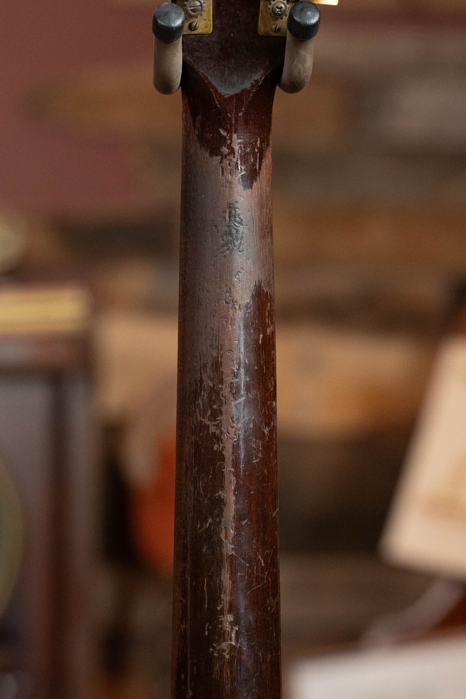 A close-up of the worn, scratched neck of a 1933 Gibson LOO Adirondack/Mahogany OO Tobacco Sunburst Acoustic Guitar (#550) by Gibson, set against a blurred, warm-toned rustic wood background—a classic vintage detail.