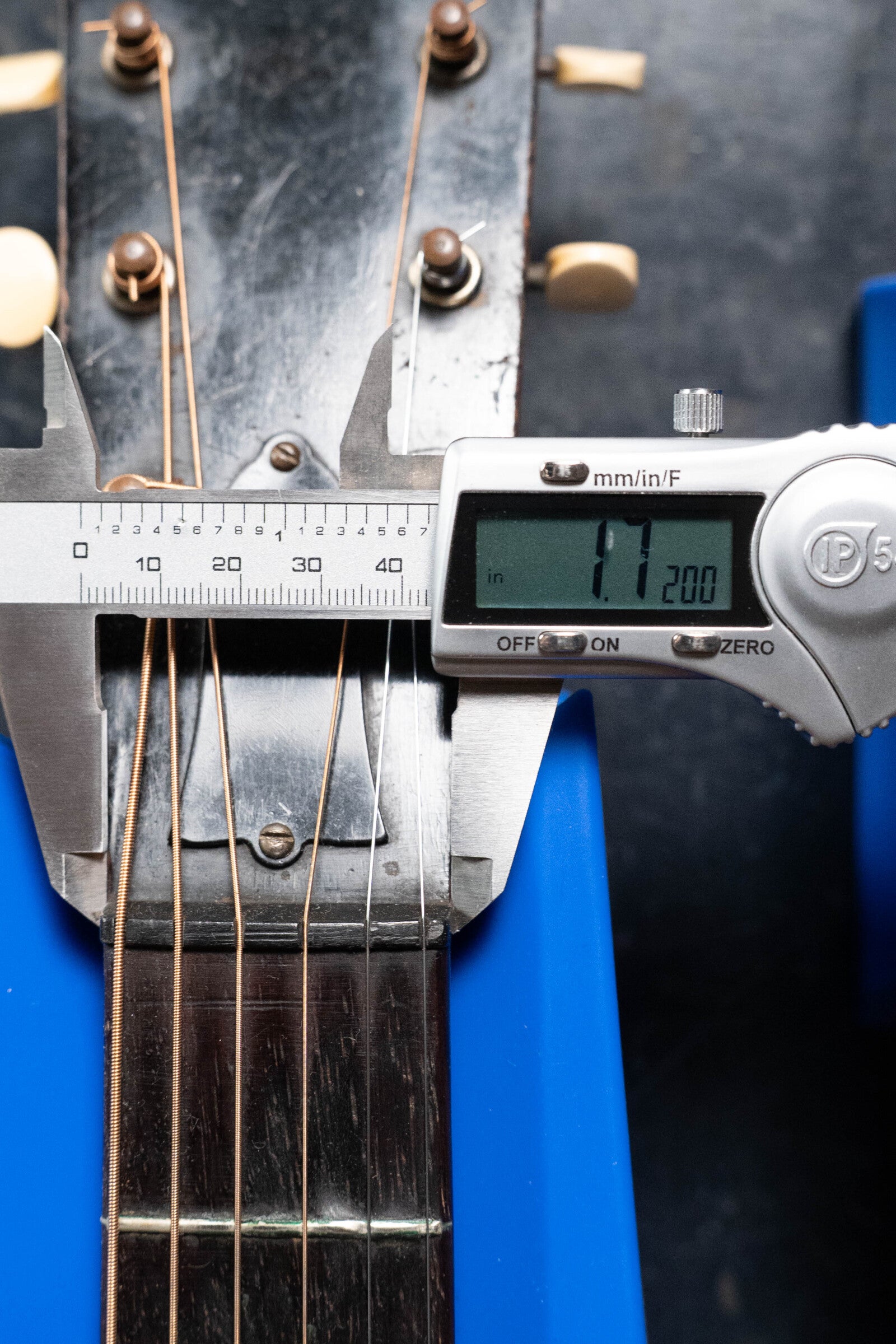 A digital caliper measures the neck width of a (Used) 1933 Gibson LOO Adirondack/Mahogany OO Tobacco Sunburst Acoustic Guitar #550 by Gibson near the headstock, reading 1.200 inches. The guitar has metal strings, tuning pegs, and blue supports.