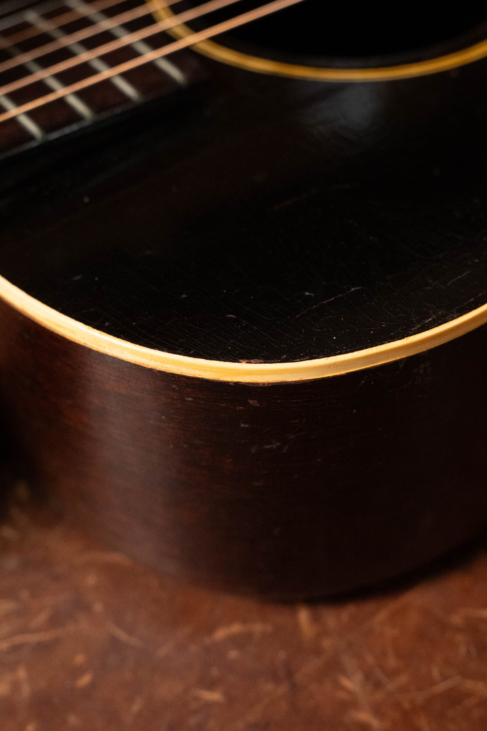 Close-up of a (Used) 1933 Gibson LOO Adirondack/Mahogany OO Tobacco Sunburst Acoustic Guitar #550 shows dark wood grain, cream edge binding, and part of the strings and fretboard on a brown textured surface. Brand: Gibson.