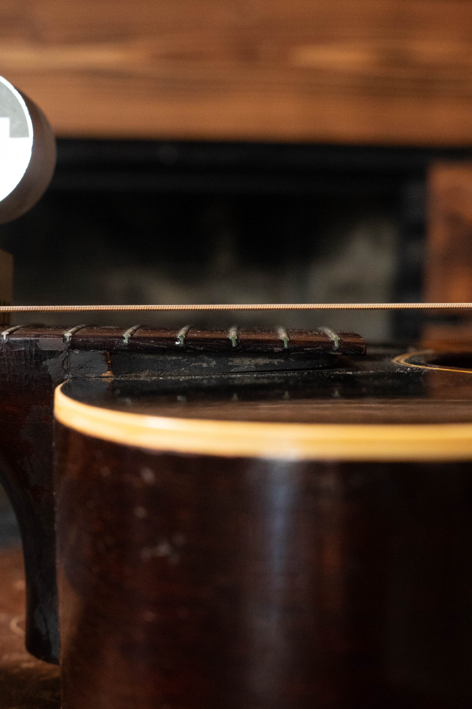 Close-up side view of a (Used) 1933 Gibson LOO Adirondack/Mahogany OO Tobacco Sunburst Acoustic Guitar #550 by Gibson, highlighting the body, neck, strings, and frets with a blurred background.