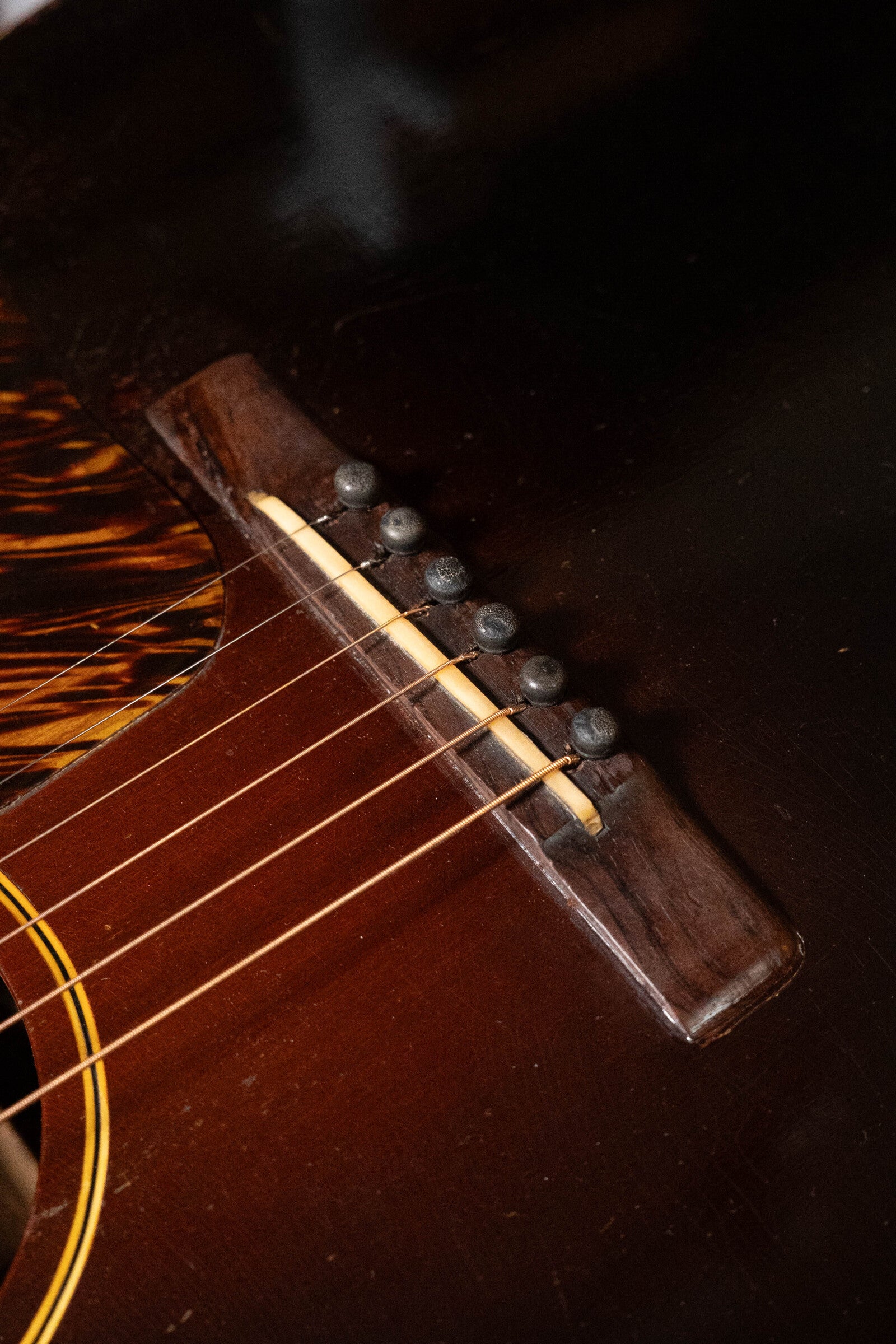 Close-up of the bridge and strings on a used 1933 Gibson LOO Adirondack/Mahogany OO Tobacco Sunburst Acoustic Guitar, highlighting the dark wood, bridge pins, and glossy body.