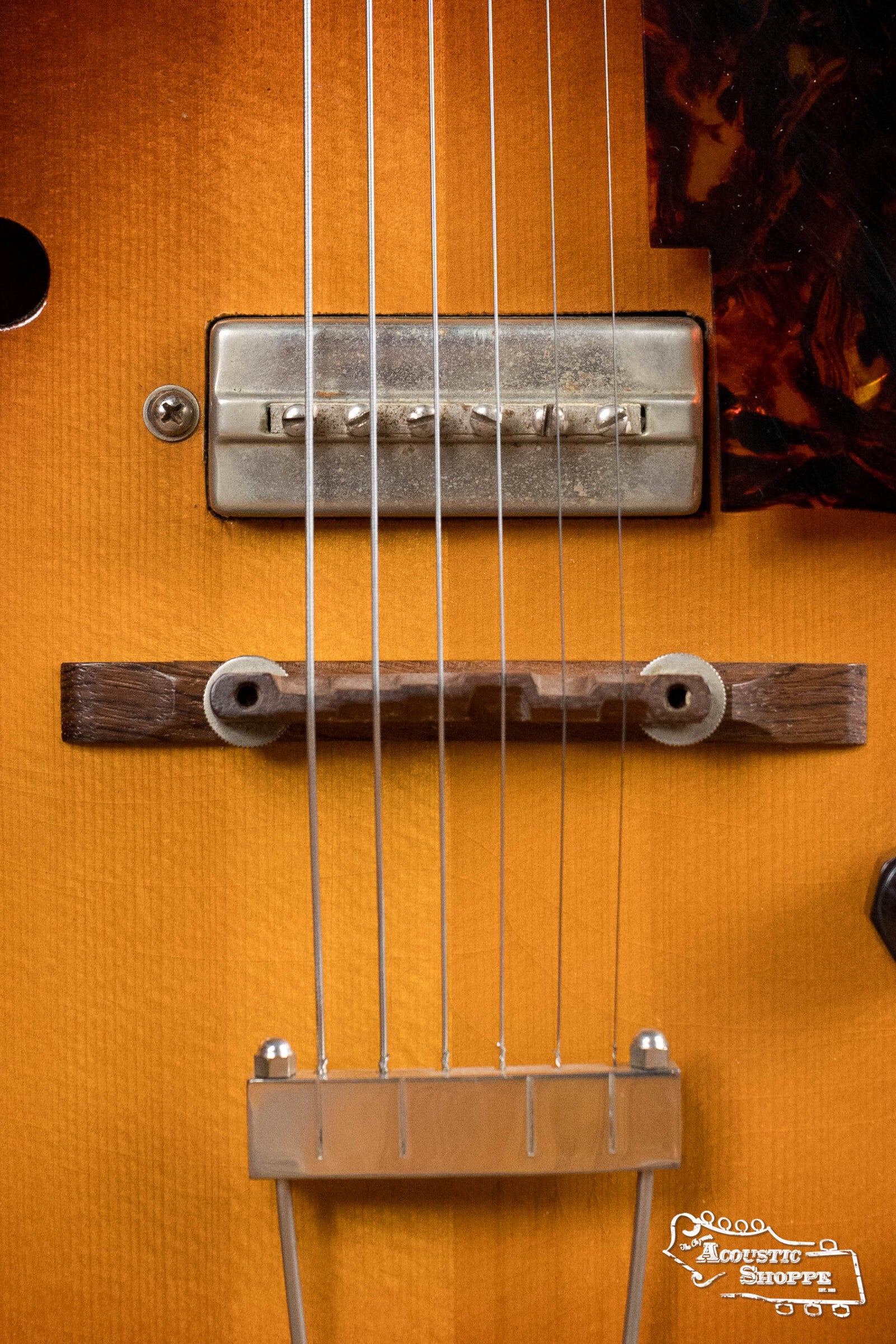 Close-up of a (Used) 1942 Gibson ES-125 hollow-body guitar by Gibson, featuring metal strings, P-90 pickup, wooden bridge, part of a tortoiseshell pickguard on glossy amber finish. "Acoustic Shoppe" logo appears at the bottom right.