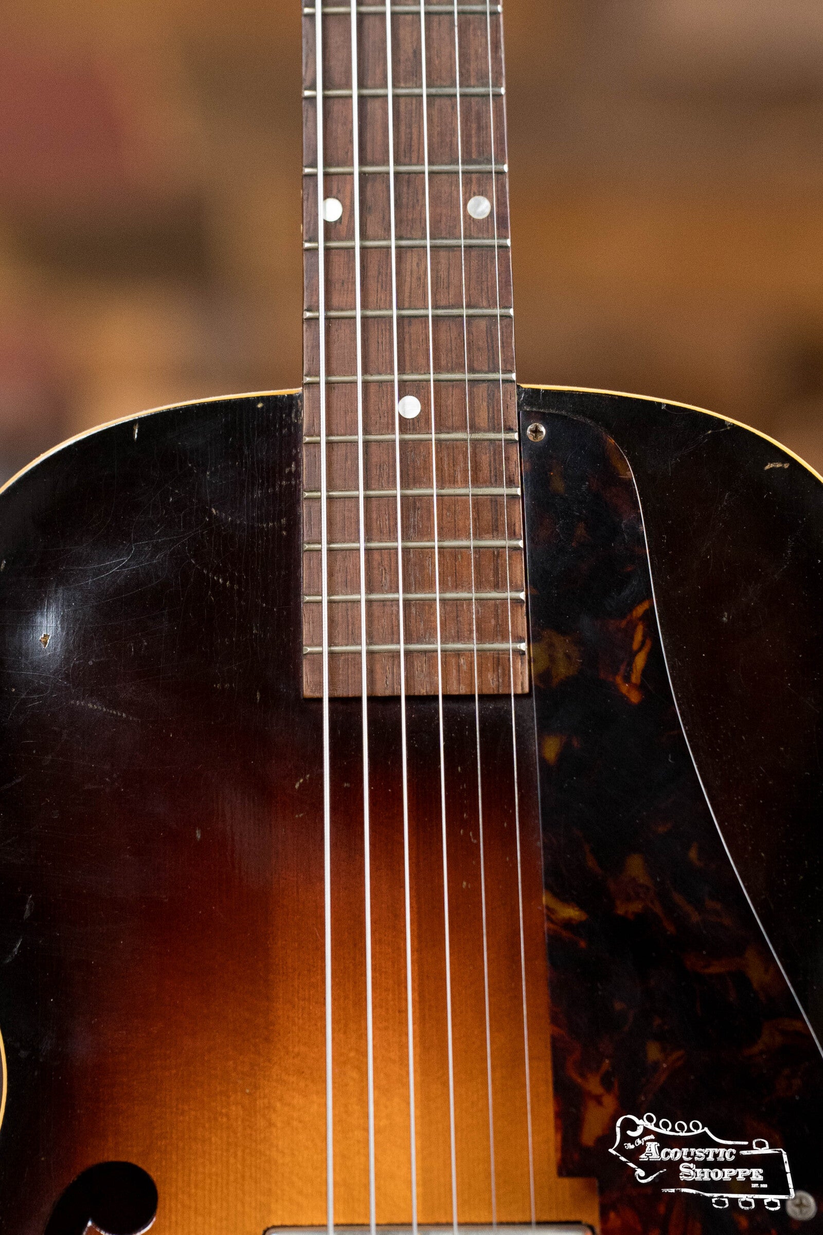 Close-up of a (Used) 1942 Gibson ES-125 by Gibson, highlighting its hollow-body design, sunburst finish, P-90 pickup, fretboard, strings, and tortoiseshell pickguard with Acoustic Shoppe logo in the lower right corner.