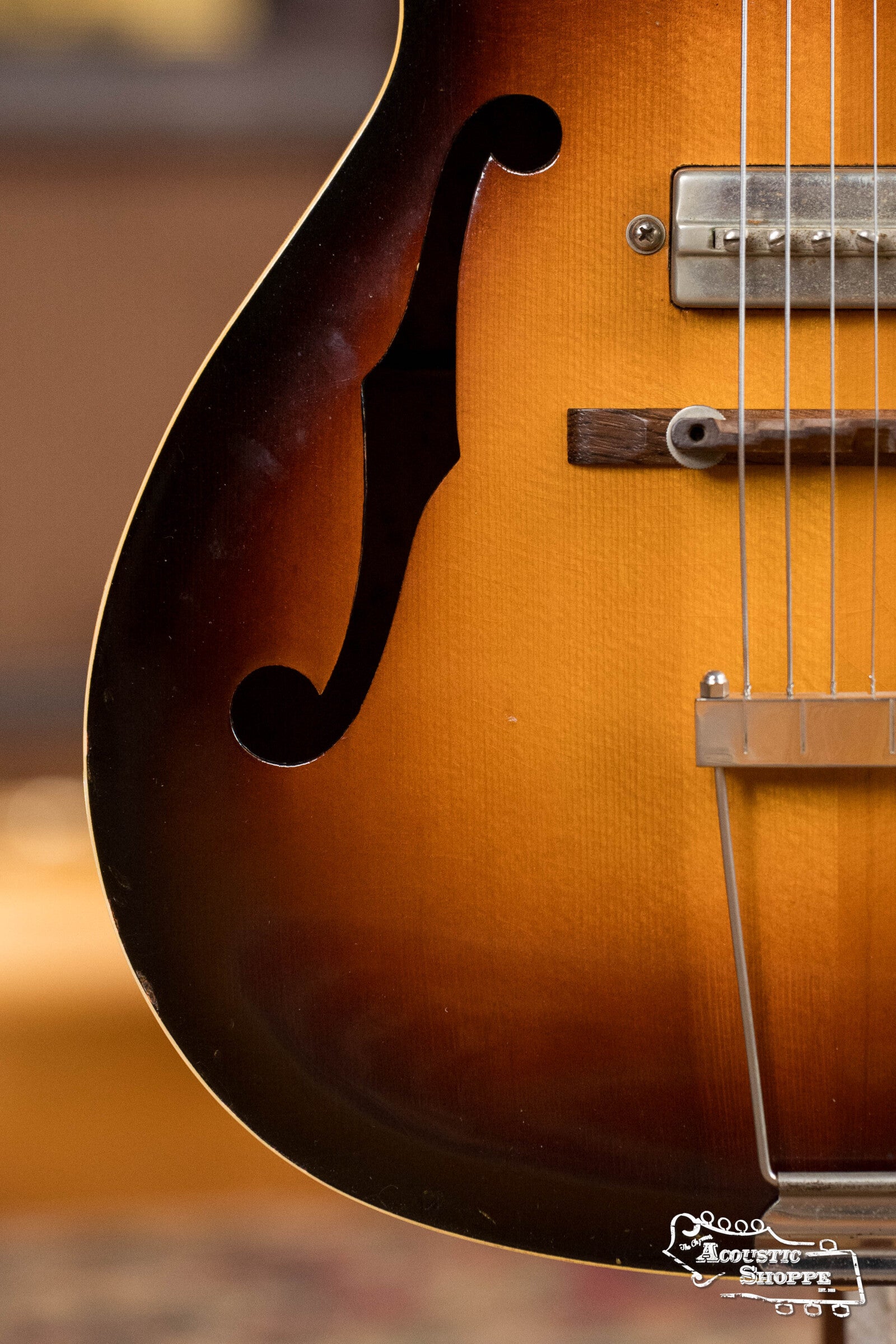 Close-up of a (Used) 1942 Gibson ES-125 by Gibson, highlighting the hollow-body's f-hole, bridge, strings, and pickguard in warm lighting that accentuates the wood grain.