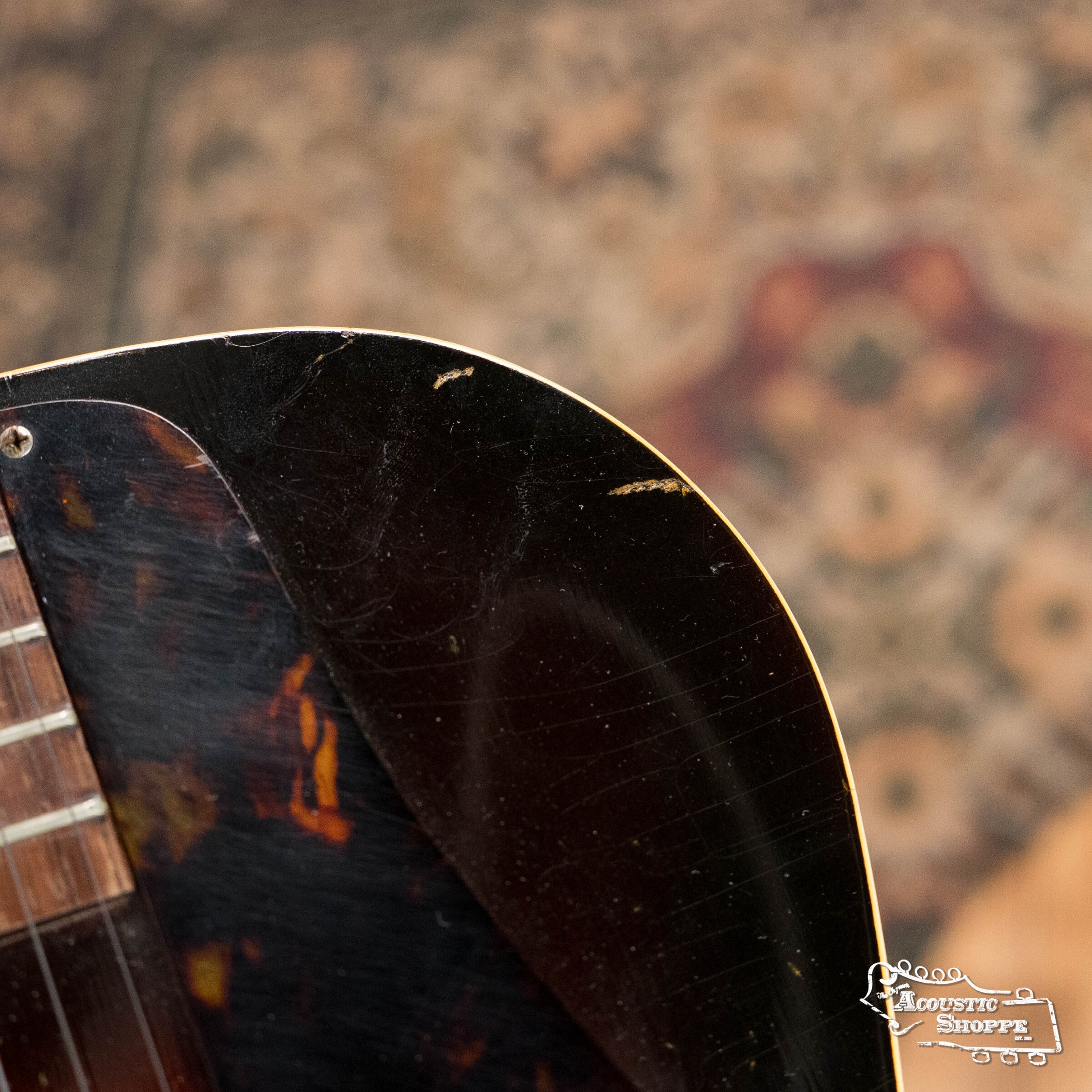Close-up of a (Used) 1942 Gibson ES-125 by Gibson shows part of the fretboard, pickguard, and P-90 pickup. Minor scratches and edge wear are visible, set against an out-of-focus patterned rug background.