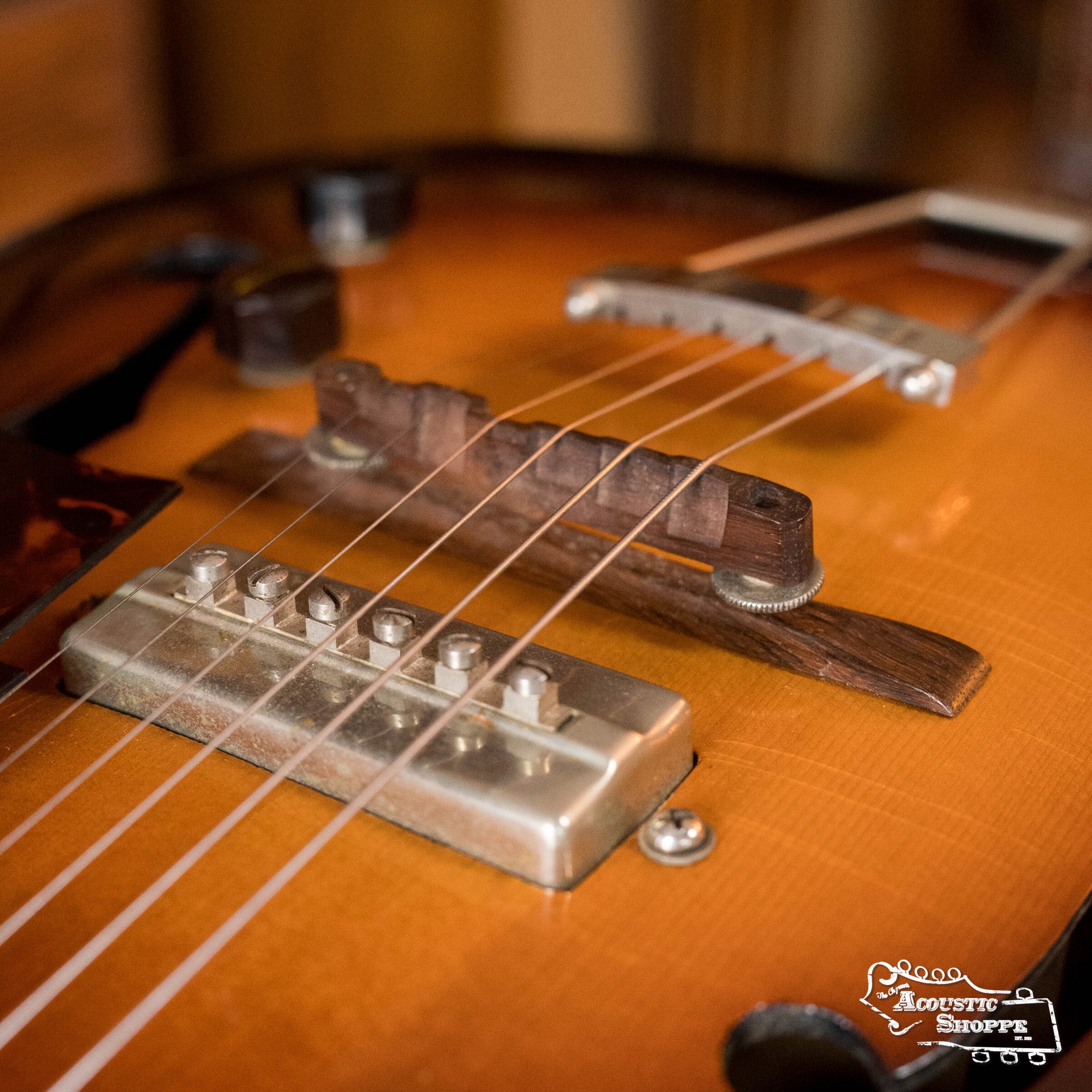 Close-up of a (Used) 1942 Gibson ES-125’s bridge, strings, and P-90 pickup by Gibson, displaying wood grain and sound hole details; The Acoustic Shoppe logo appears in the lower right corner.