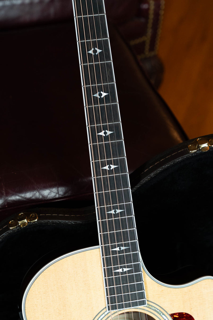 Detailed view of the (Used) 1999 Taylor Guitars 814-BCE 25th Anniversary Sitka/Rosewood Grand Auditorium Guitar #4124, highlighting bird inlays on the fretboard as it rests in its case atop a dark leather chair with brass studs.