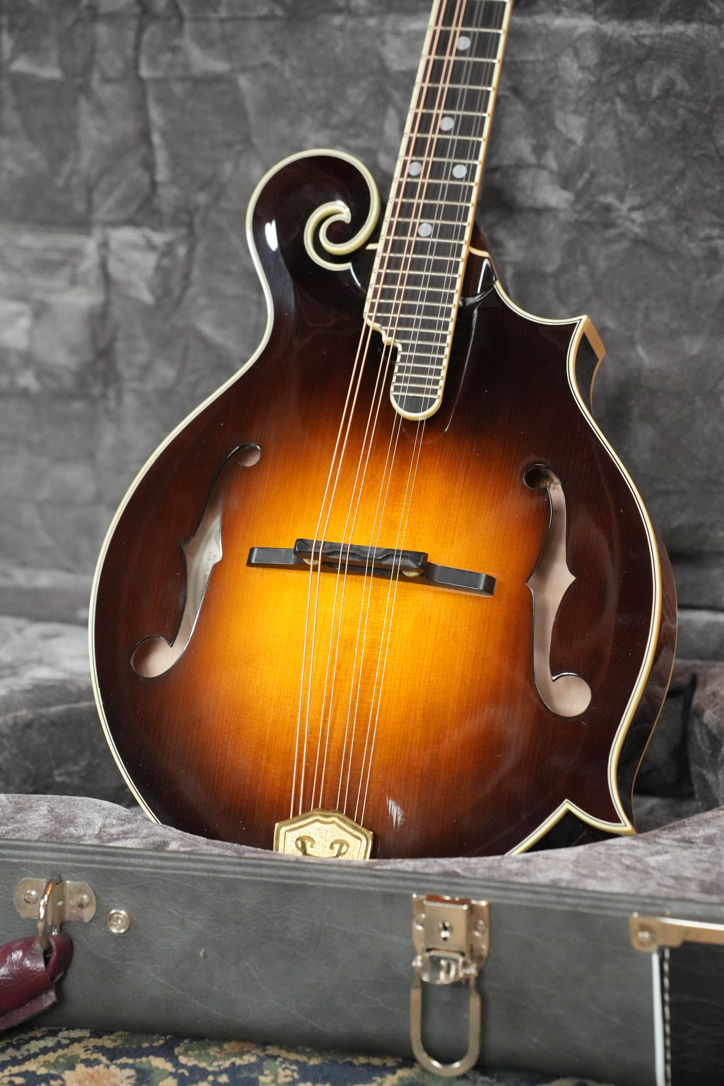 A used 2009 Weber Fern Spruce/Maple F-Style Mandolin (#7602) with a sunburst finish and ivory binding rests in a gray, plush-lined hard case, showcasing boutique luthiery from Weber.