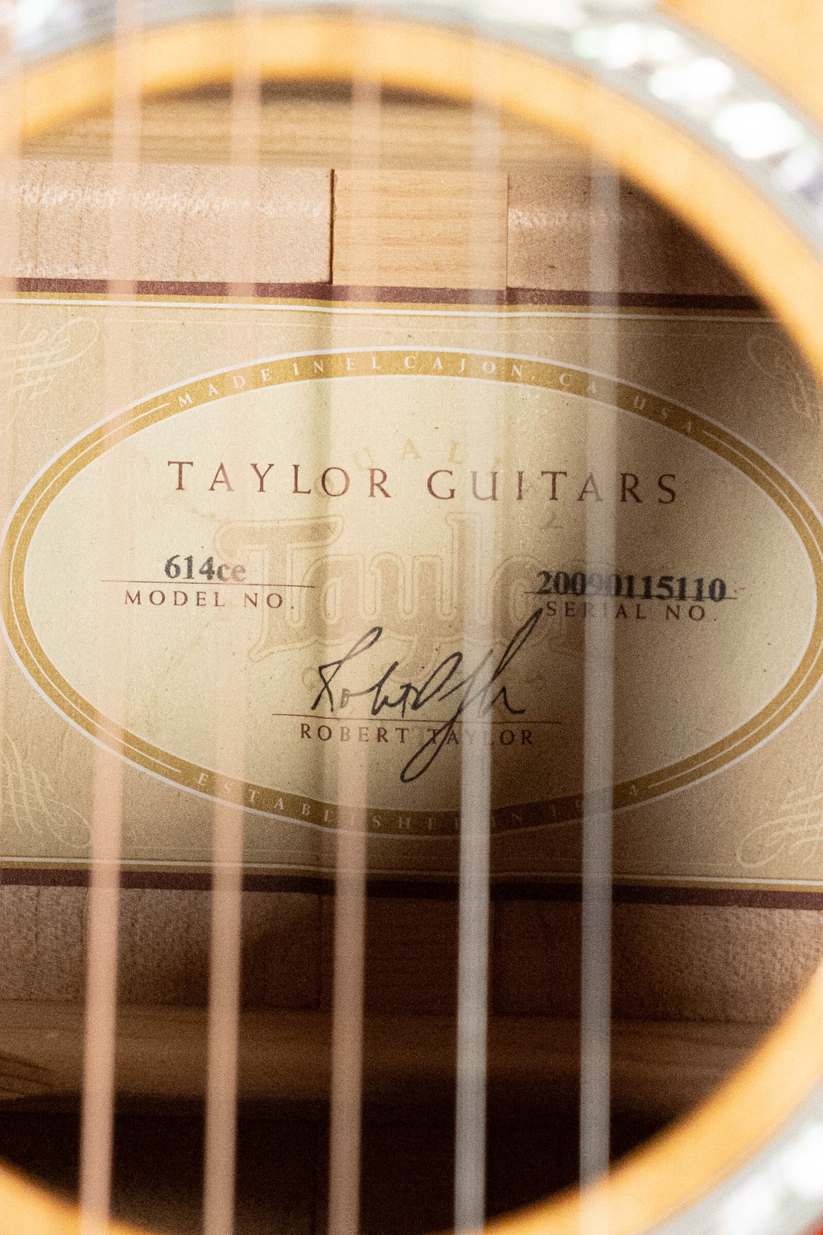 Close-up of a (Used) 2009 Taylor Guitars 614CE Torrefied Sitka/Maple Grand Auditorium Cutaway label, seen through the strings, showing model 614CE and serial #5110 with the signature on the label.