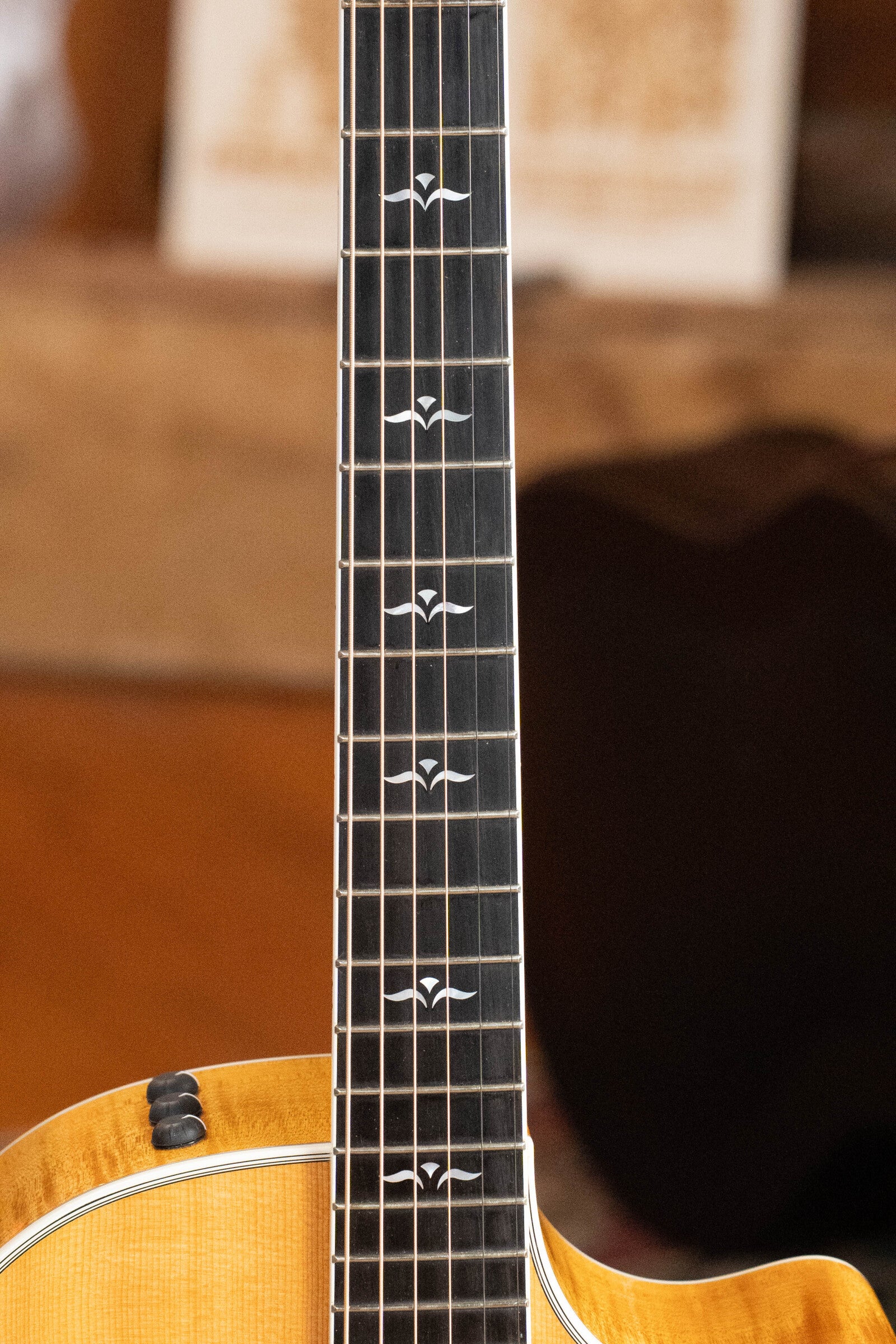 Close-up of a used 2009 Taylor Guitars 614CE Grand Auditorium #5110, featuring decorative fretboard inlays and a torrefied Sitka spruce/maple body with natural wood finish, beautifully highlighted indoors.