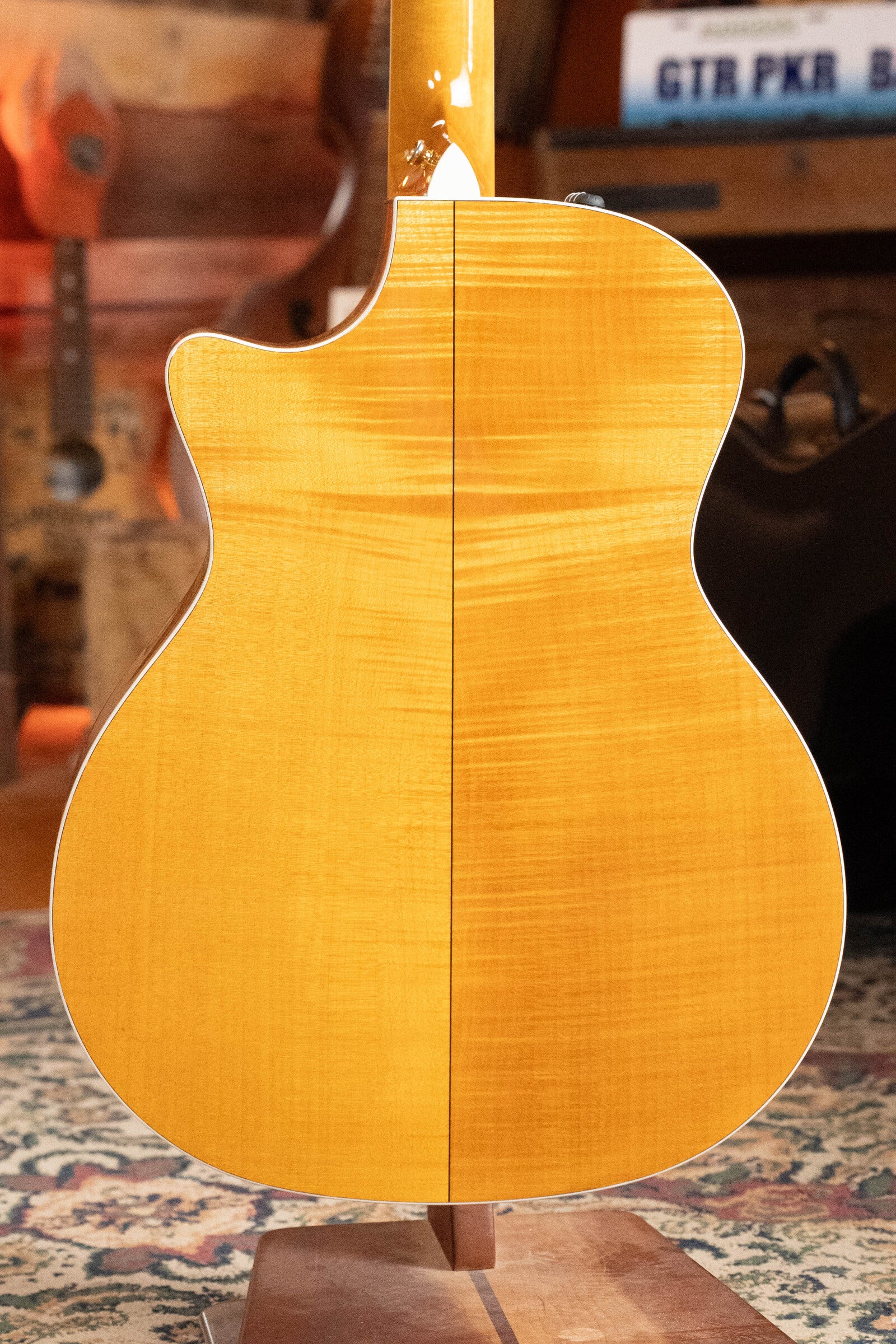 A close-up of the back of a (Used) 2009 Taylor Guitars 614CE Torrefied Sitka/Maple Cutaway Grand Auditorium Guitar w/Pickup (#5110), highlighting its wood grain and white binding, set in a cozy, rustic room.