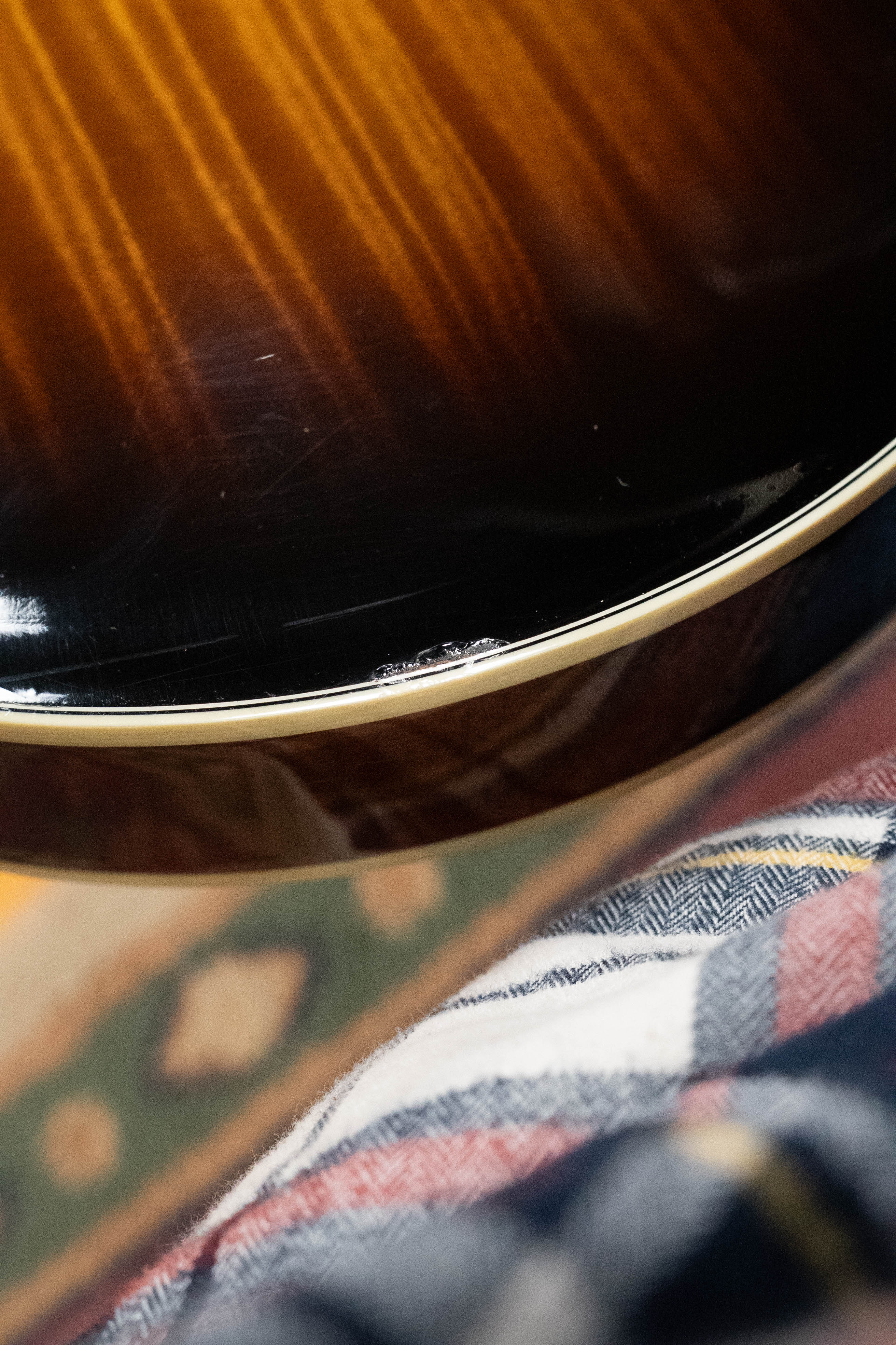 Close-up of a glossy Weber 2016 Fern A-Style Mandolin (Red Spruce/Flamed Maple) resting on a lap, with part of a patterned rug and plaid fabric in the background.