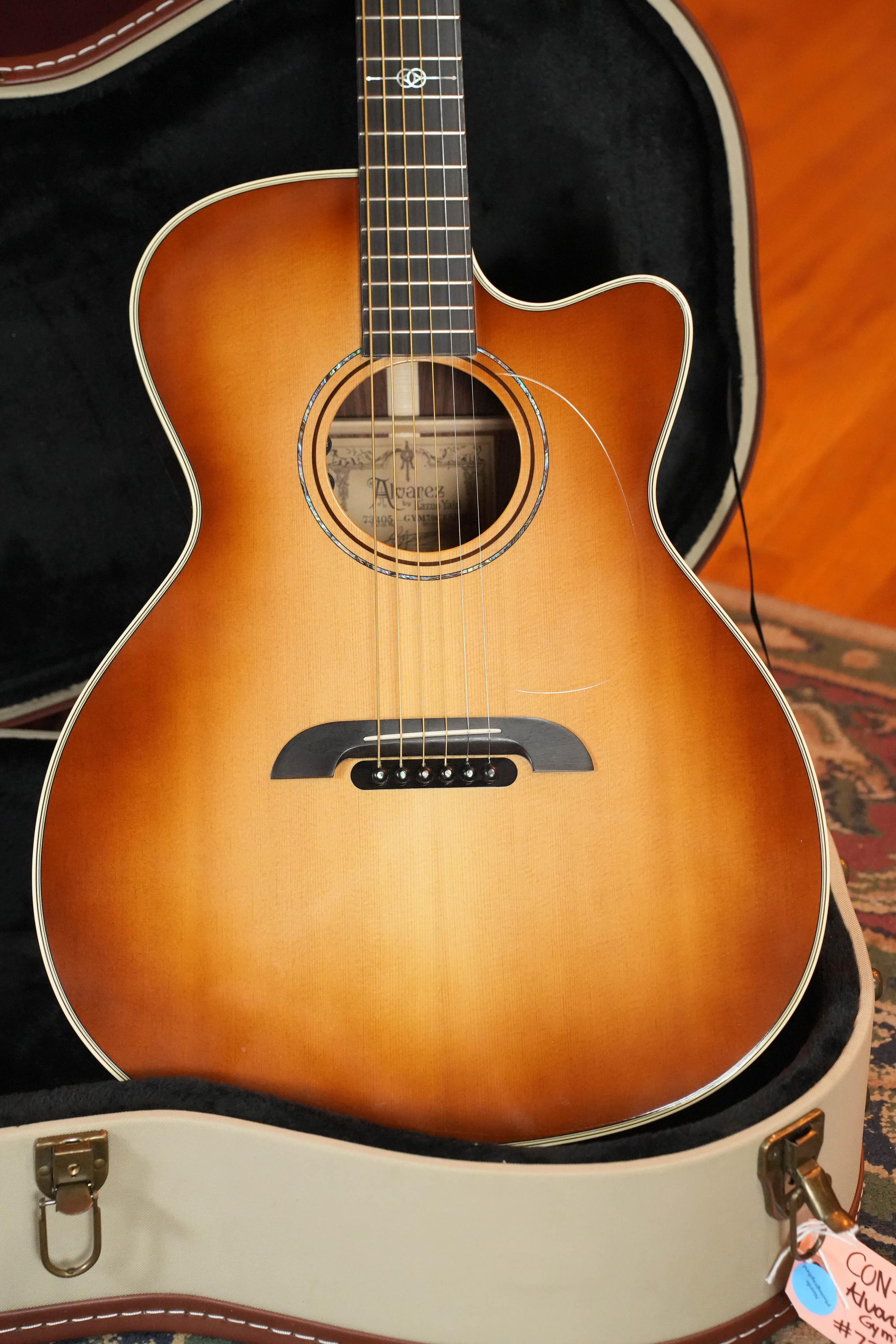 A (Used) 2018 Alvarez Yairi GYM70CESHB Grand Auditorium Acoustic Guitar w/ LR Baggs VTC from The Acoustic Shoppe rests in an open hard case, displaying its sunburst finish and black bridge, with a price tag partially visible.