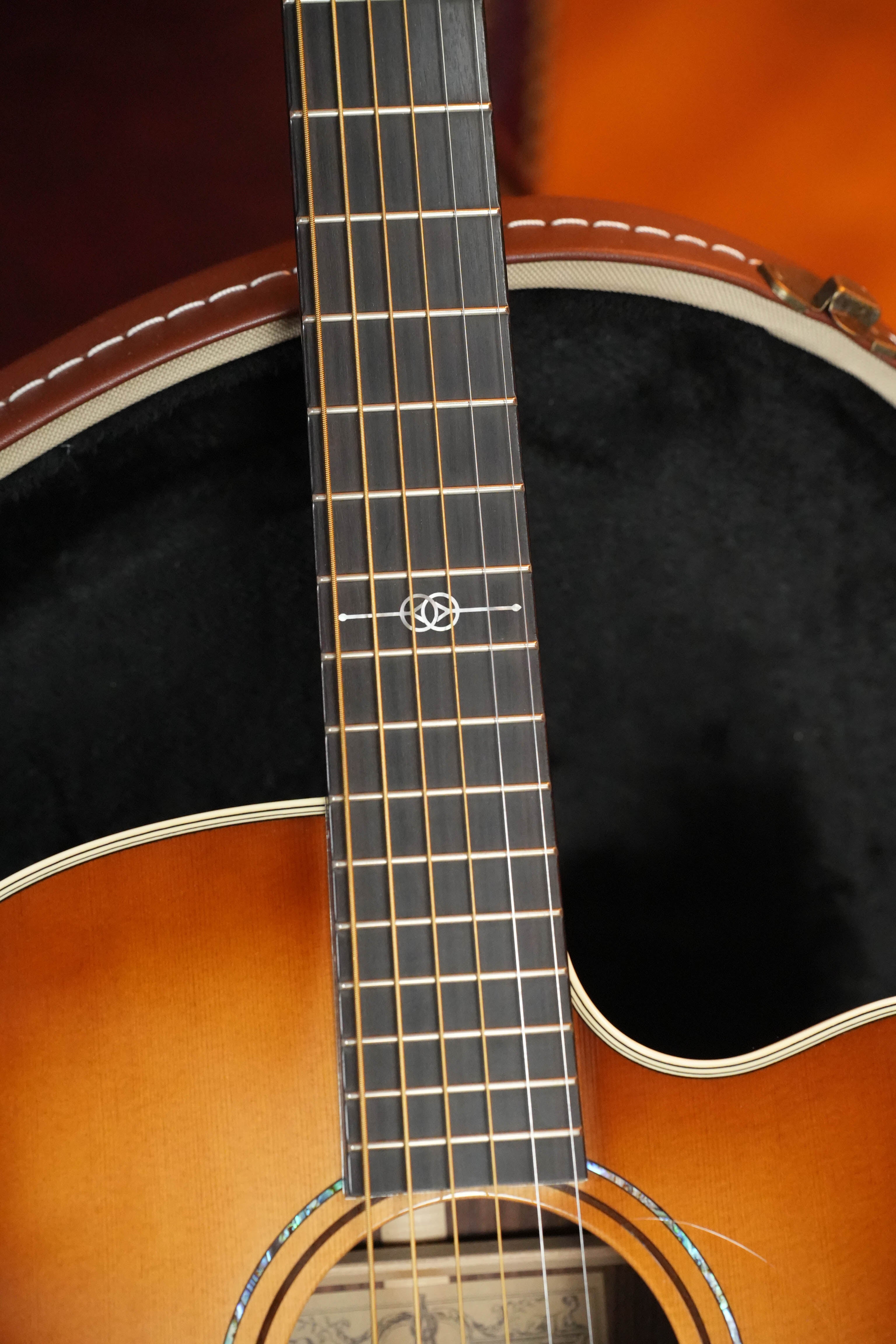 A close-up of a (Used) 2018 Alvarez Yairi GYM70CESHB Grand Auditorium Acoustic Guitar’s neck and upper body from The Acoustic Shoppe, featuring fretboard inlay, with the LR Baggs VTC case lined in black fabric visible in the background.