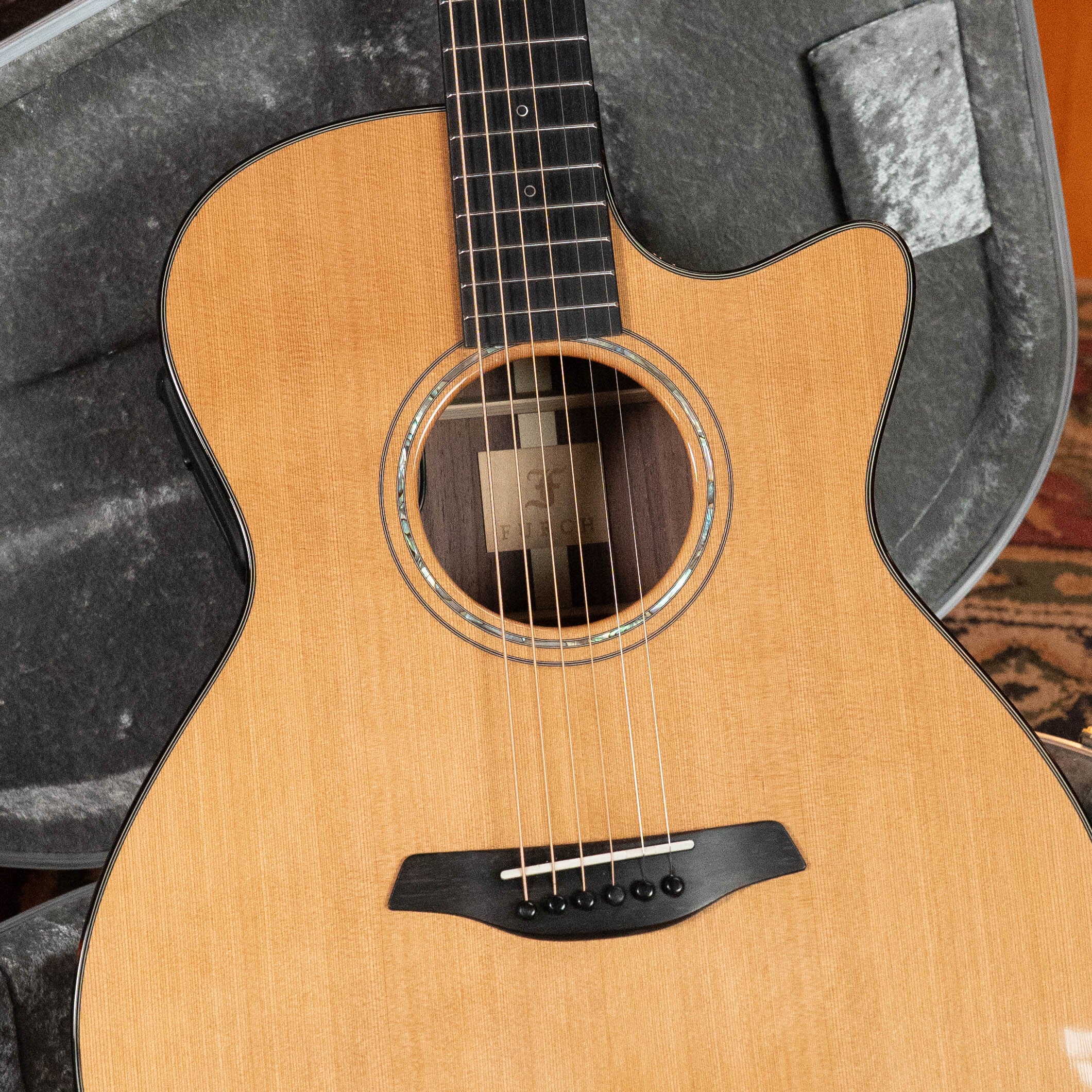 Close-up of a (Used) 2020 Furch Yellow Gc-CR Red Cedar/Rosewood Grand Auditorium Acoustic Guitar #3716 with natural finish, black bridge, and cutaway body in an open gray hard case on a patterned rug. Boutique quality from Furch.