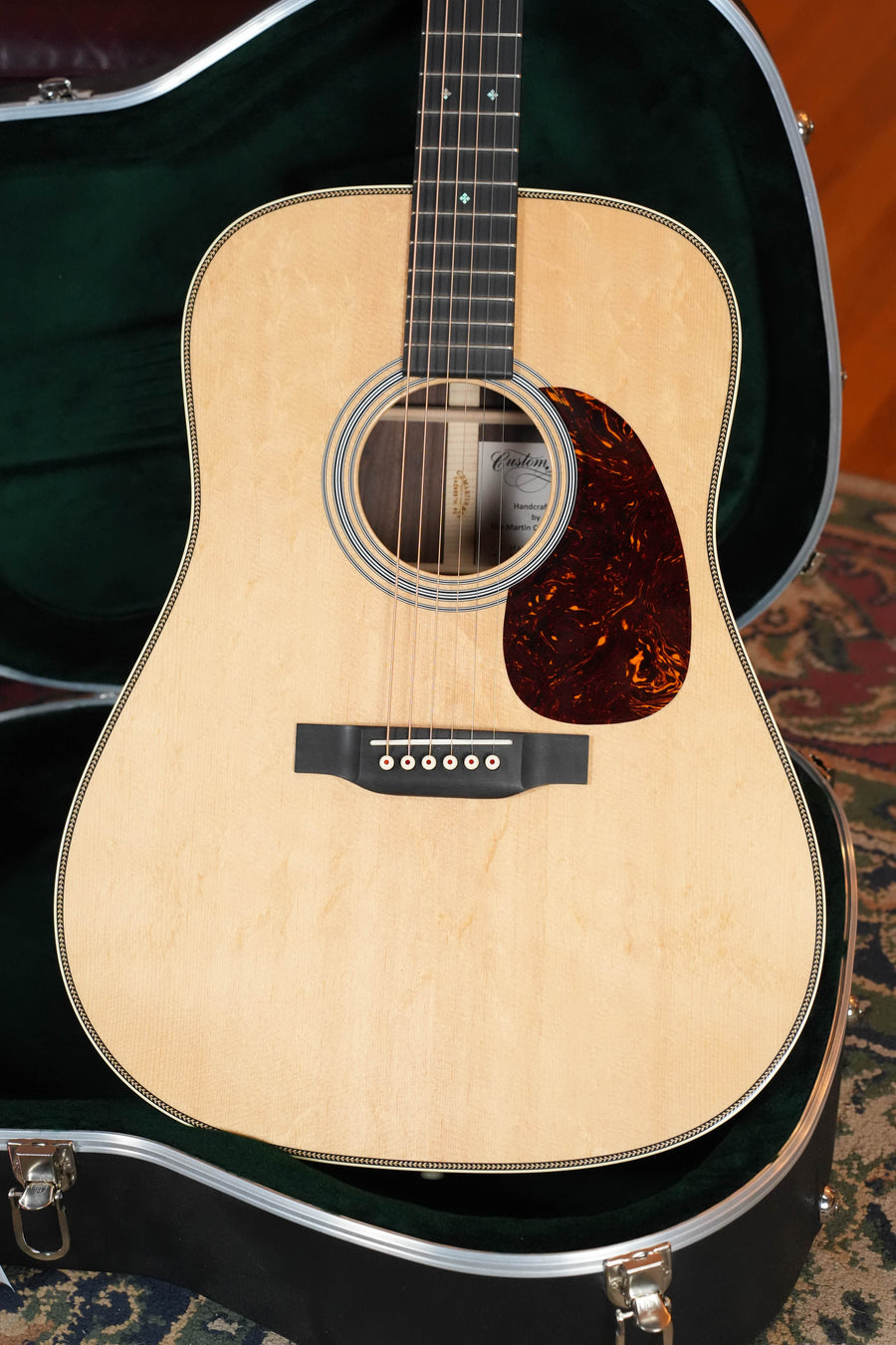 A Martin & Co. *Dread-Not Certified Used* 2021 Custom Shop HD-28 Bearclaw Sitka/East Indian Rosewood Dreadnought Acoustic Guitar #5218 rests in an open, black hard-shell case with green lining on a patterned rug.