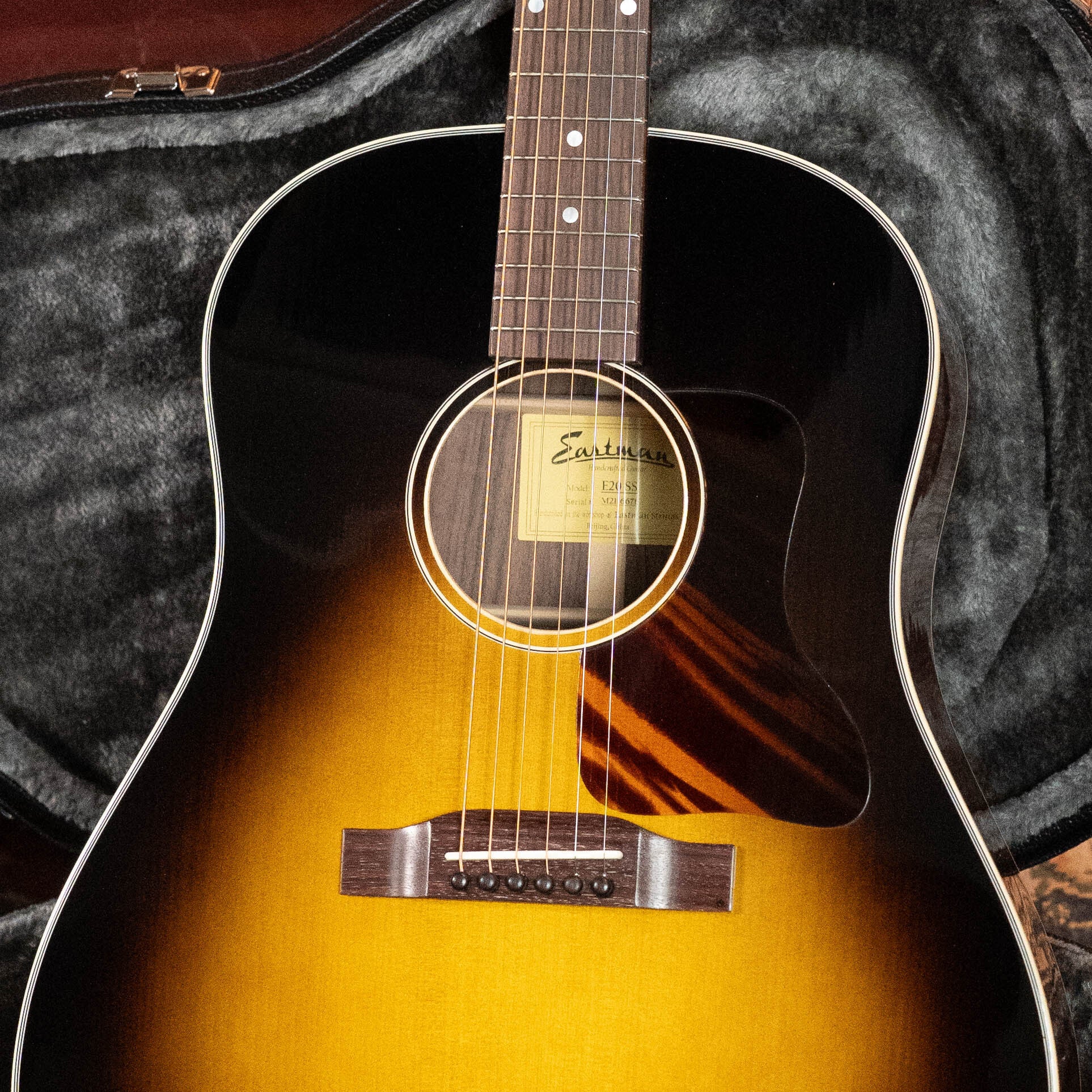 A close-up of a (Used) 2021 Eastman E20SS Adirondack/Rosewood Slope Shoulder Dreadnought Acoustic Guitar #6671 by Eastman Guitars, in a gray plush-lined hard case, showing its strings, sound hole with label, pickguard, and fretboard.