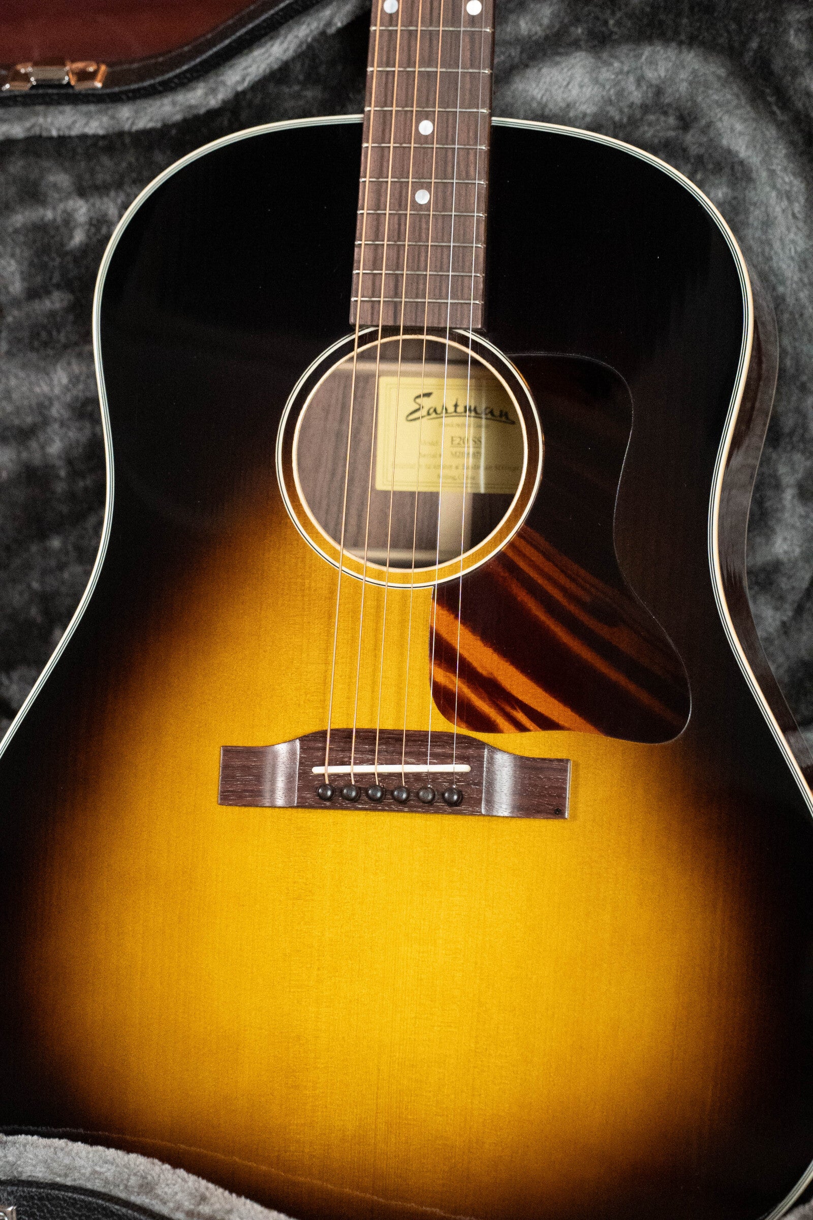 A close-up of a used 2021 Eastman Guitars E20SS Adirondack/Rosewood Slope Shoulder Dreadnought Acoustic Guitar #6671 with sunburst finish, highlighting its top, body, strings, soundhole, pickguard, and gray-lined hard case.