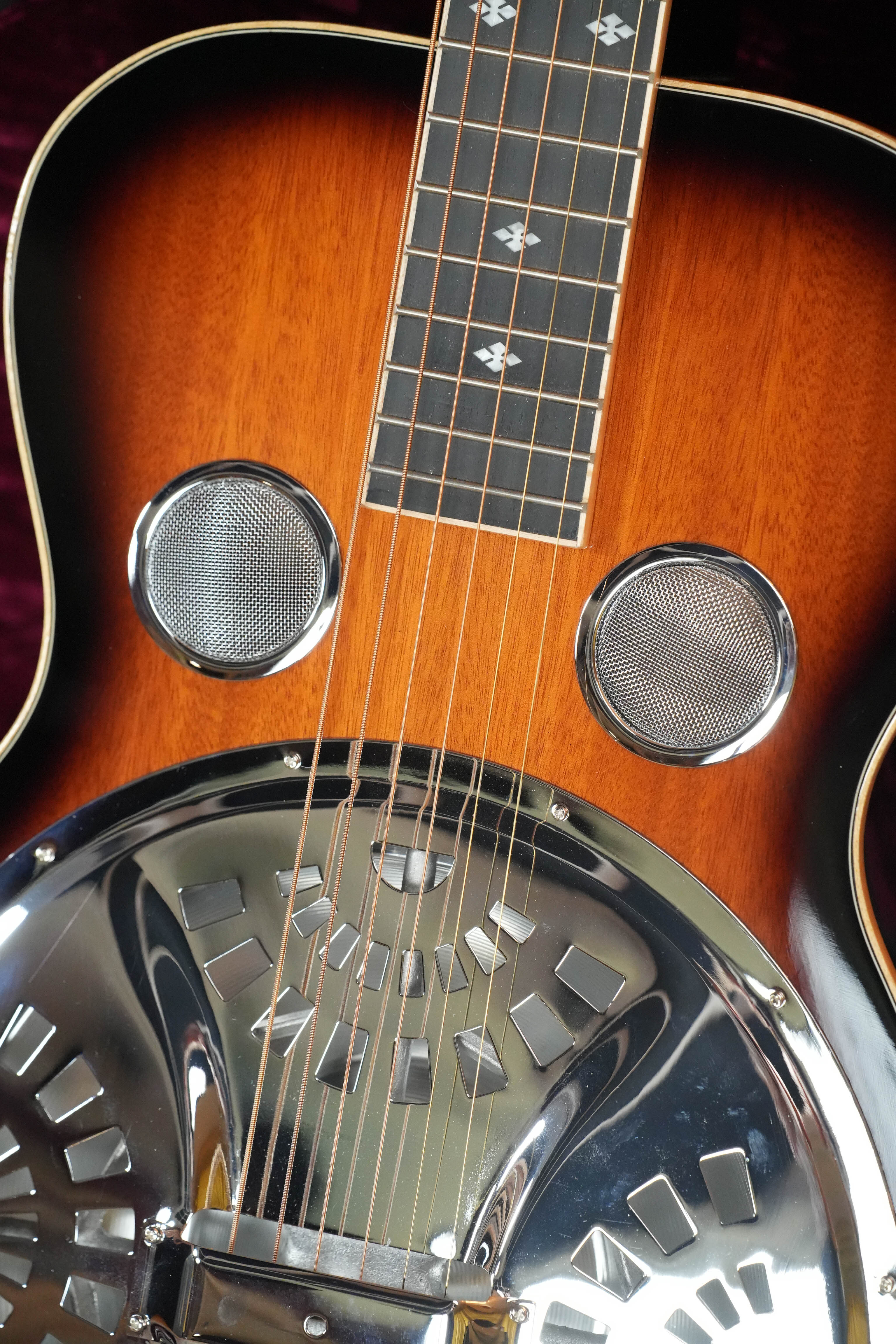 Close-up of a (Used) 2022 Gold Tone PBS-D Paul Beard Deluxe Solid Mahogany Square-Neck Resonator Guitar #8165, highlighting its metal resonator cone, sound holes, wooden body, and decorative fretboard inlays.