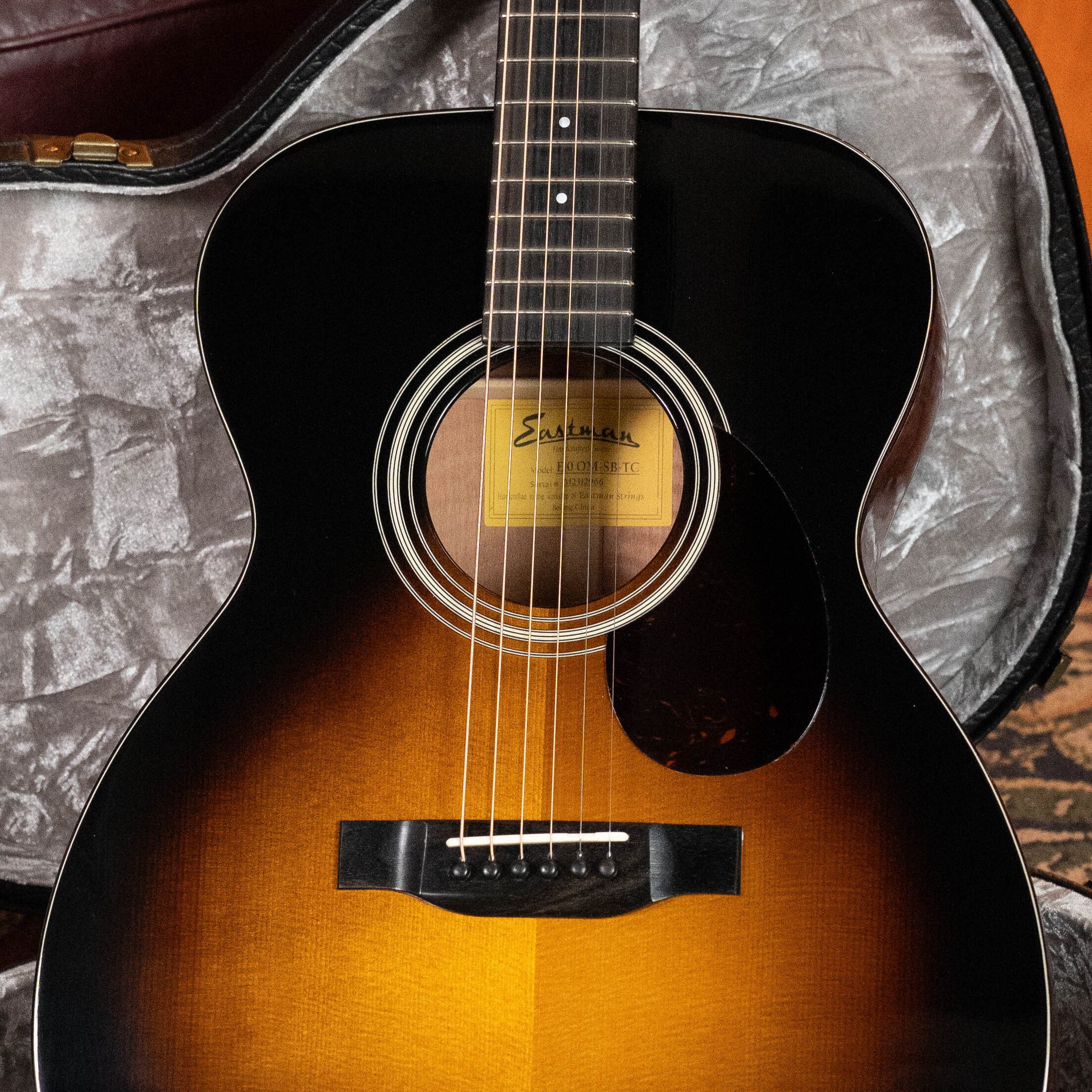 A 2023 Eastman E10OM-TC-SB Sunburst Orchestra Model #2966 with a Thermo-Cured Adirondack spruce top rests in an open gray-lined hardshell case, showing the Eastman Guitars label inside the sound hole.