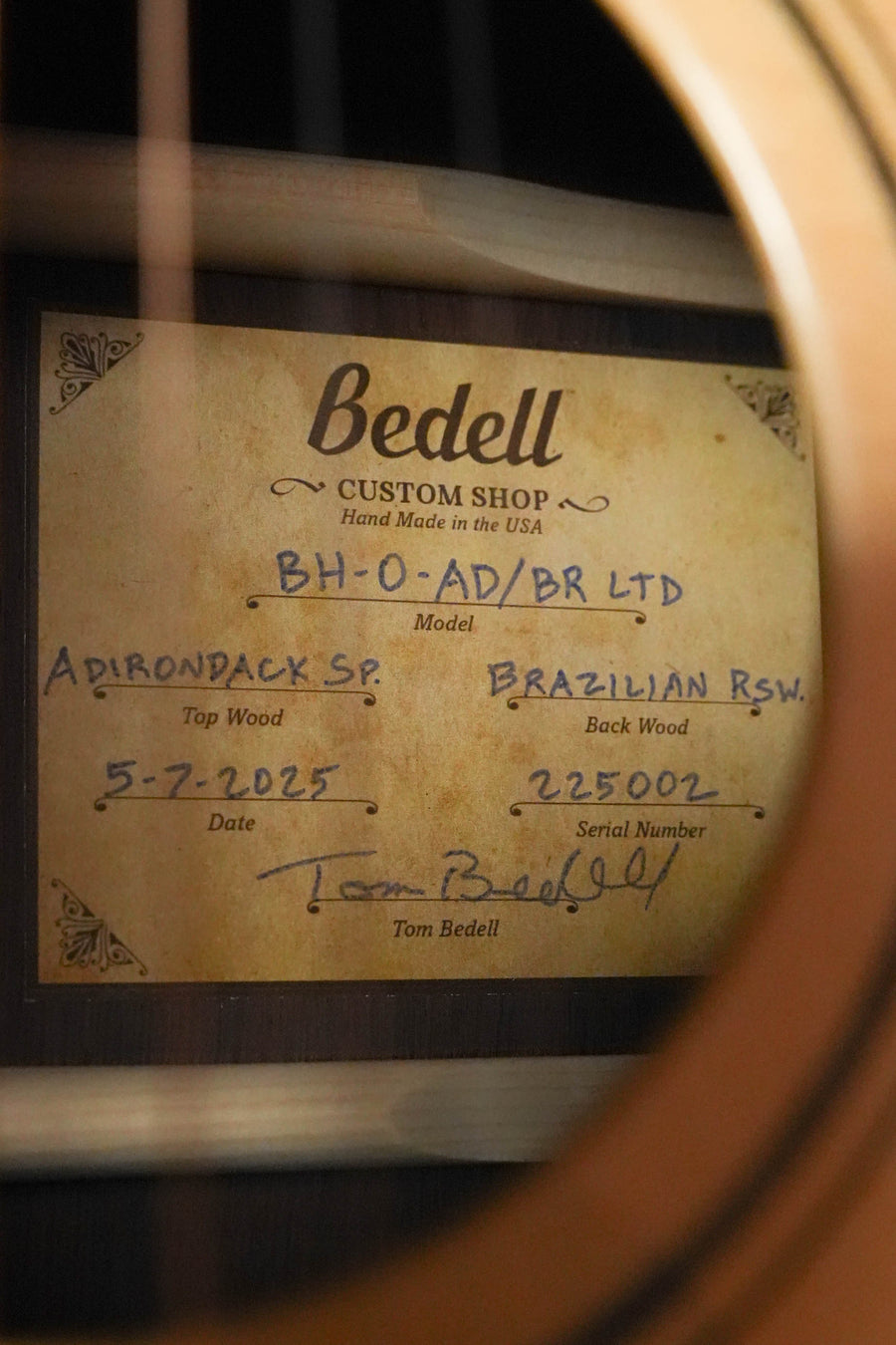 A close-up of the Bedell Guitars Bahia Limited Edition BH-O-AD/BR LTD Custom Shop OM Acoustic Guitar (#5002) label, viewed through the sound hole, details its Adirondack/Brazilian rosewood build and Tom Bedell's signature dated 5-7-2025.