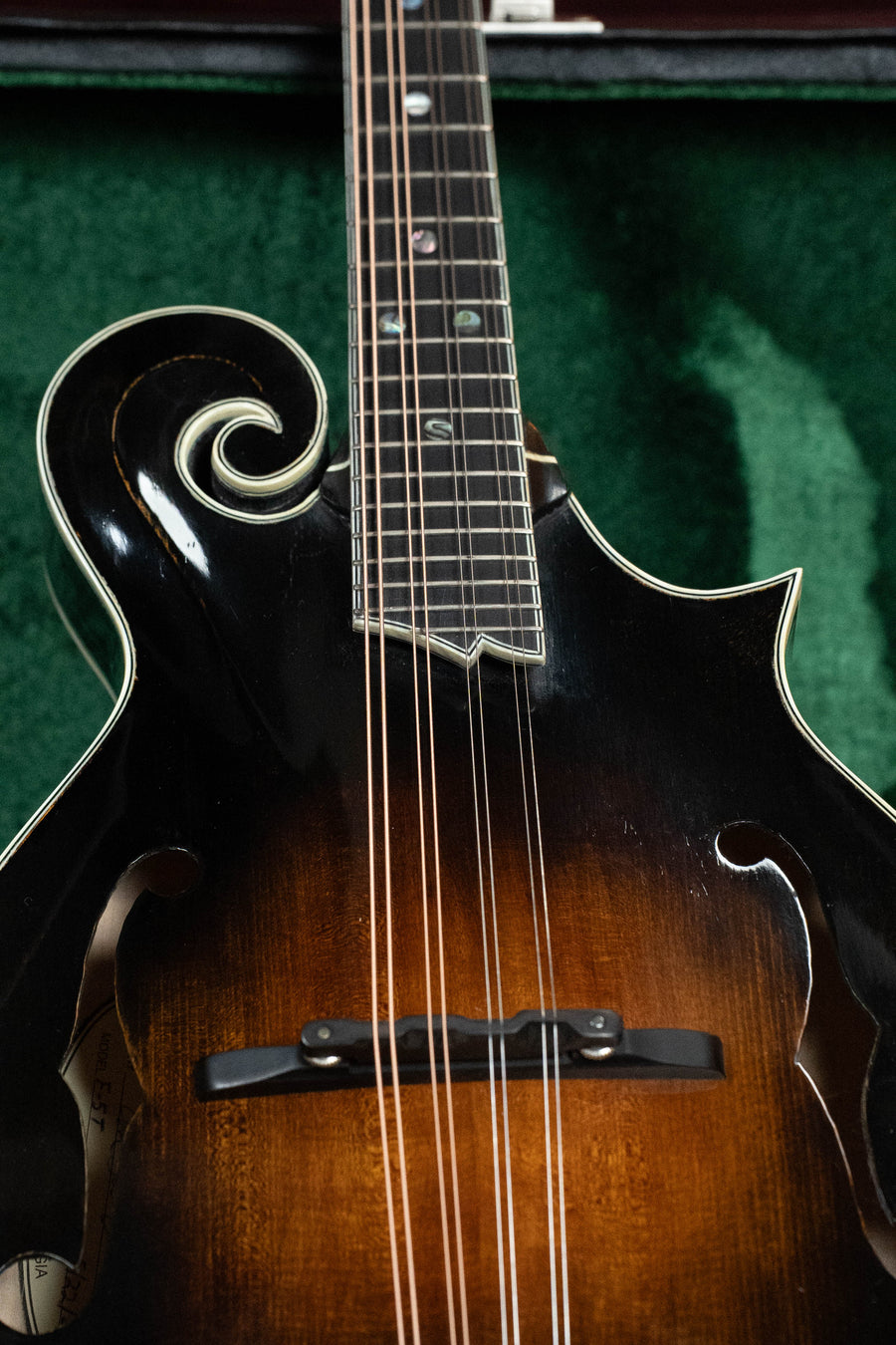 Close-up of the Buford 2025 F-5T Torrefied Adirondack/Maple hand-carved F-style mandolin (#011) with dark sunburst finish, ornate scroll, and f-holes, resting in a green velvet-lined case—a top bluegrass instrument.