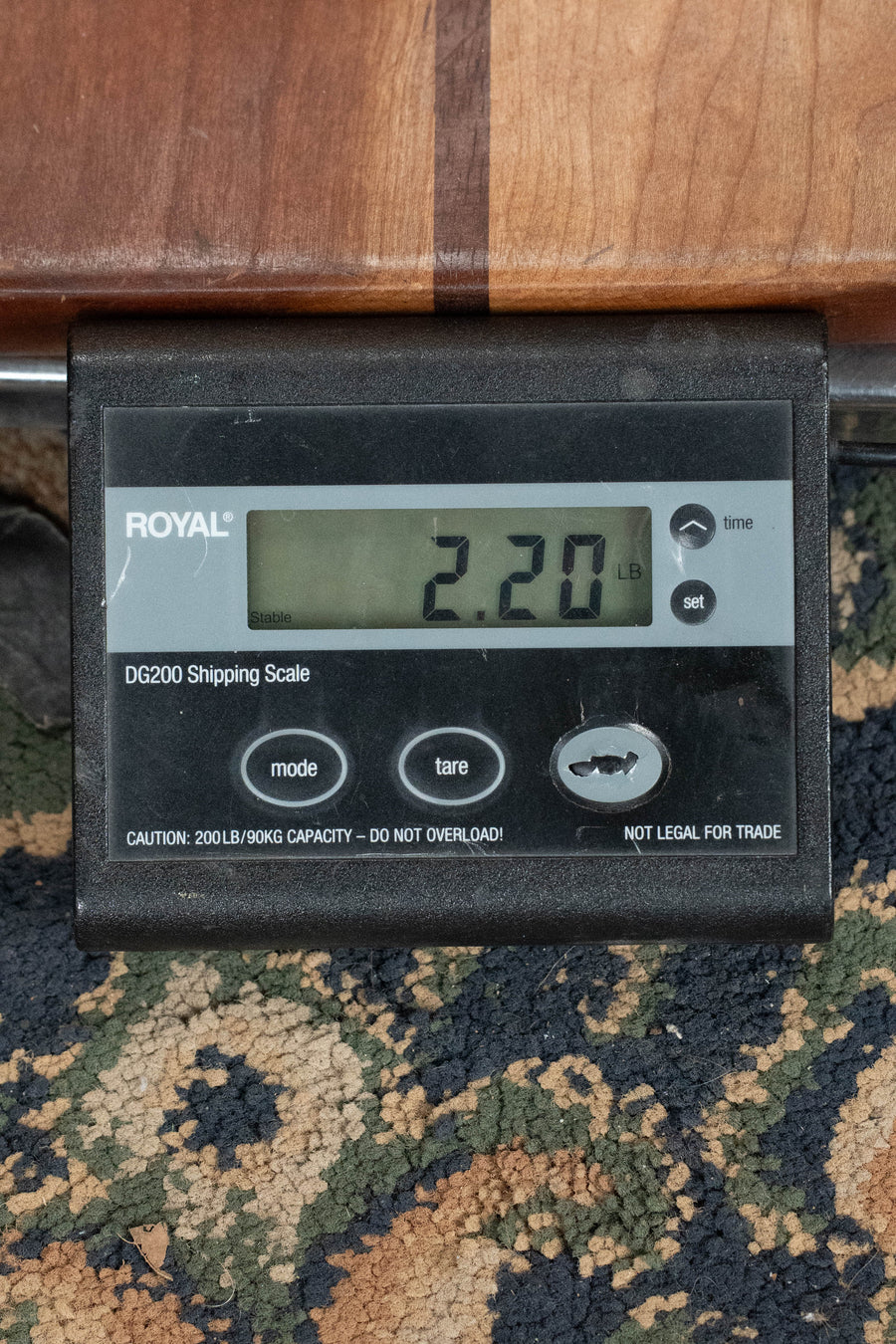 A digital shipping scale displays 2.20 pounds, supporting a Buford F-5T Torrefied Adirondack/Maple F-Style Hand-Carved Mandolin (#011) from Buford, resting on a patterned carpet with part of the instrument visible above.