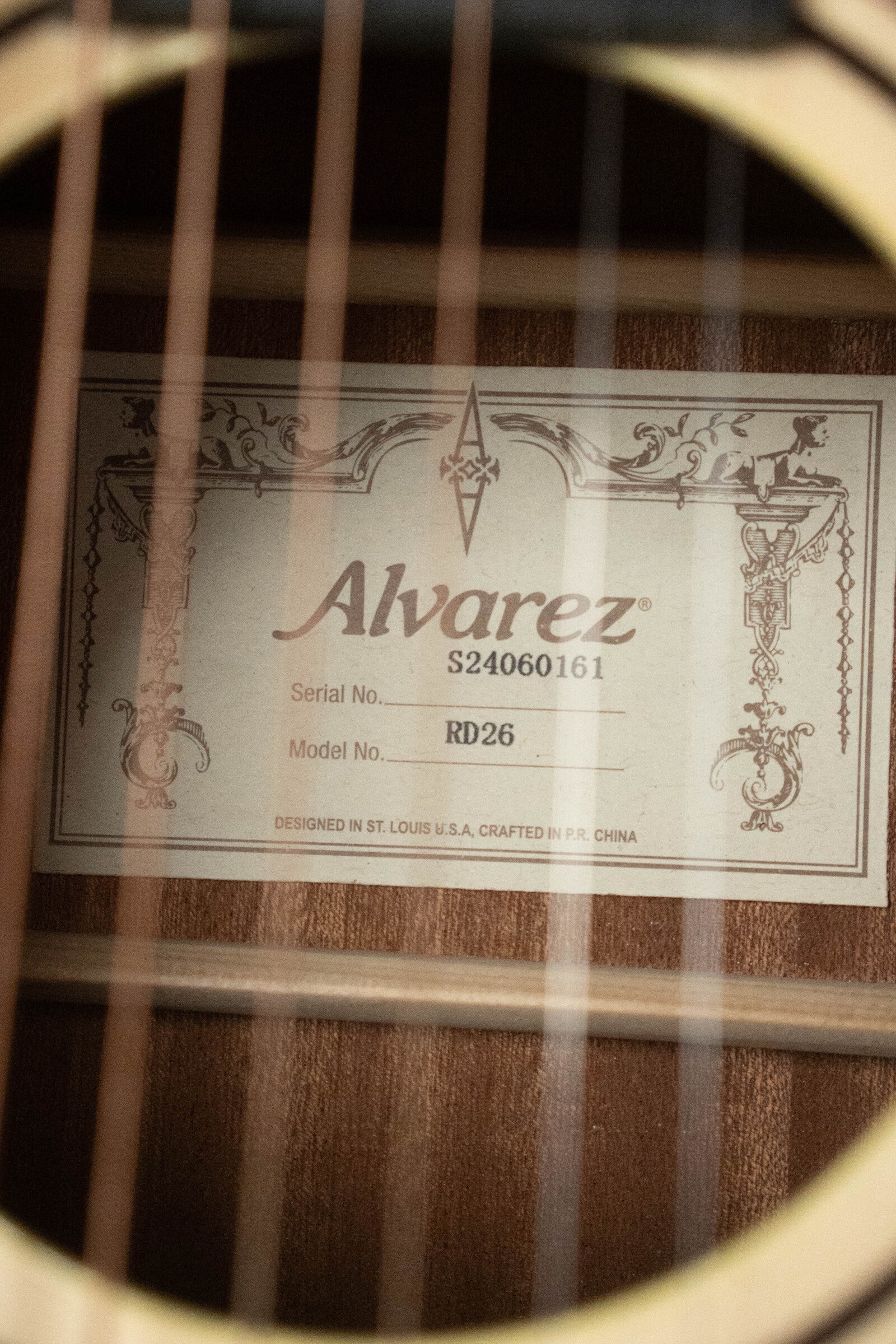 Close-up of a student-friendly (Used) 2025 Alvarez RD-26 Spruce/Mahogany Dreadnought Acoustic Guitar #0161s interior label, showing the Alvarez brand, distinctive model details, and decorative borders behind the strings.