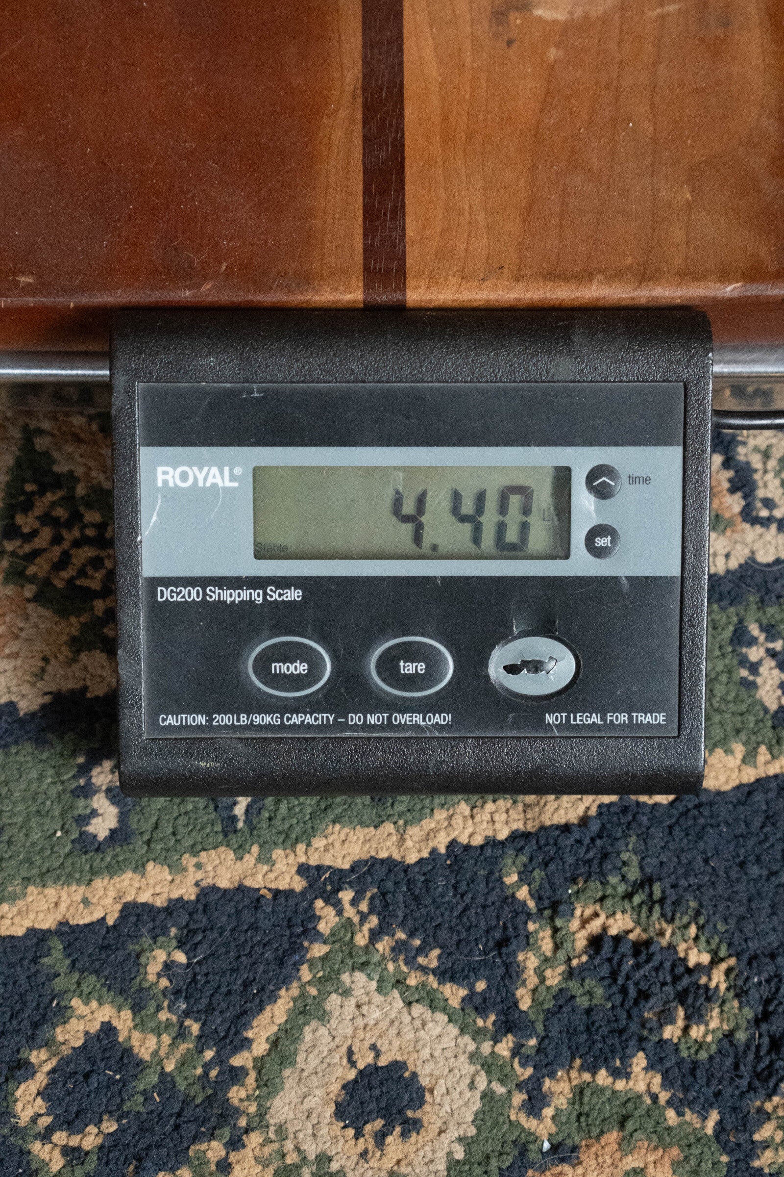 A digital shipping scale shows 4.40 lbs. On a patterned rug below part of an Alvarez (Used) 2025 RD-26 Spruce/Mahogany Dreadnought Acoustic Guitar #0161 by Alvarez, visible above a wooden surface.