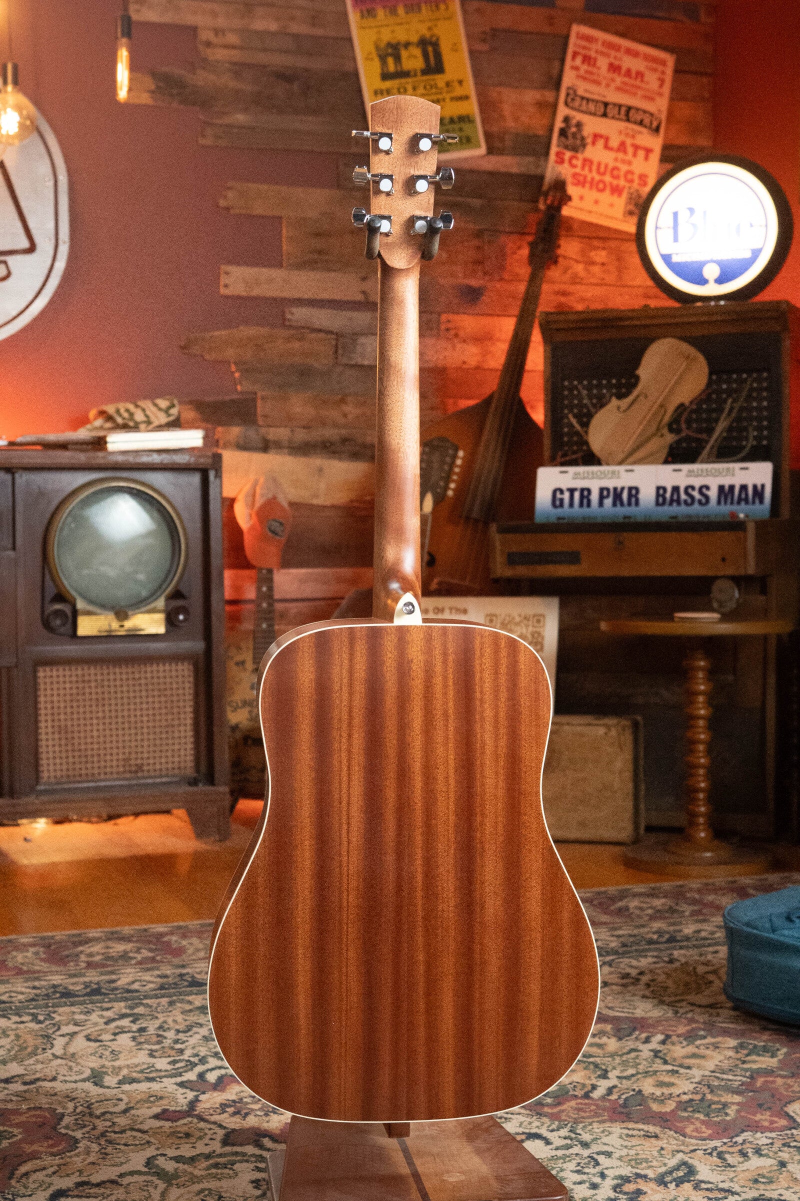 The (Used) 2025 Alvarez RD-26 Spruce/Mahogany Dreadnought Acoustic Guitar #0161 by Alvarez is shown from the back in a cozy, vintage-inspired room with warm lighting, retro TV, musical instruments, posters, and decorative signs in the background.