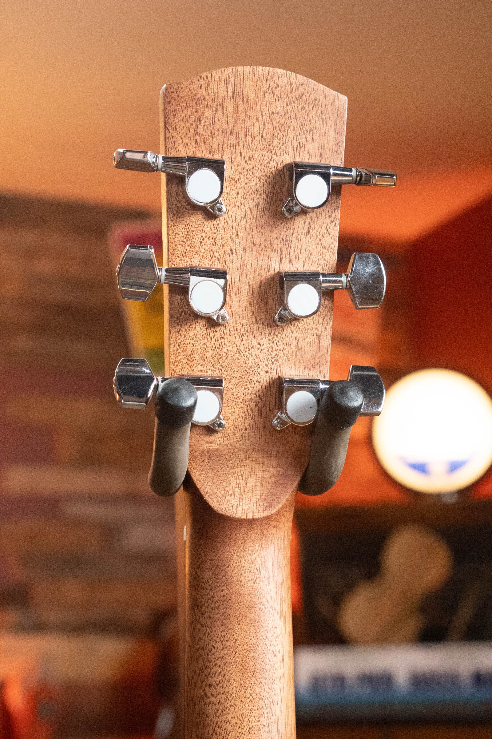The image features the back of an Alvarez (Used) 2025 RD-26 Spruce/Mahogany Dreadnought Acoustic Guitar #0161 headstock with six metal tuners, set against a warm, blurred orange and brown indoor background.