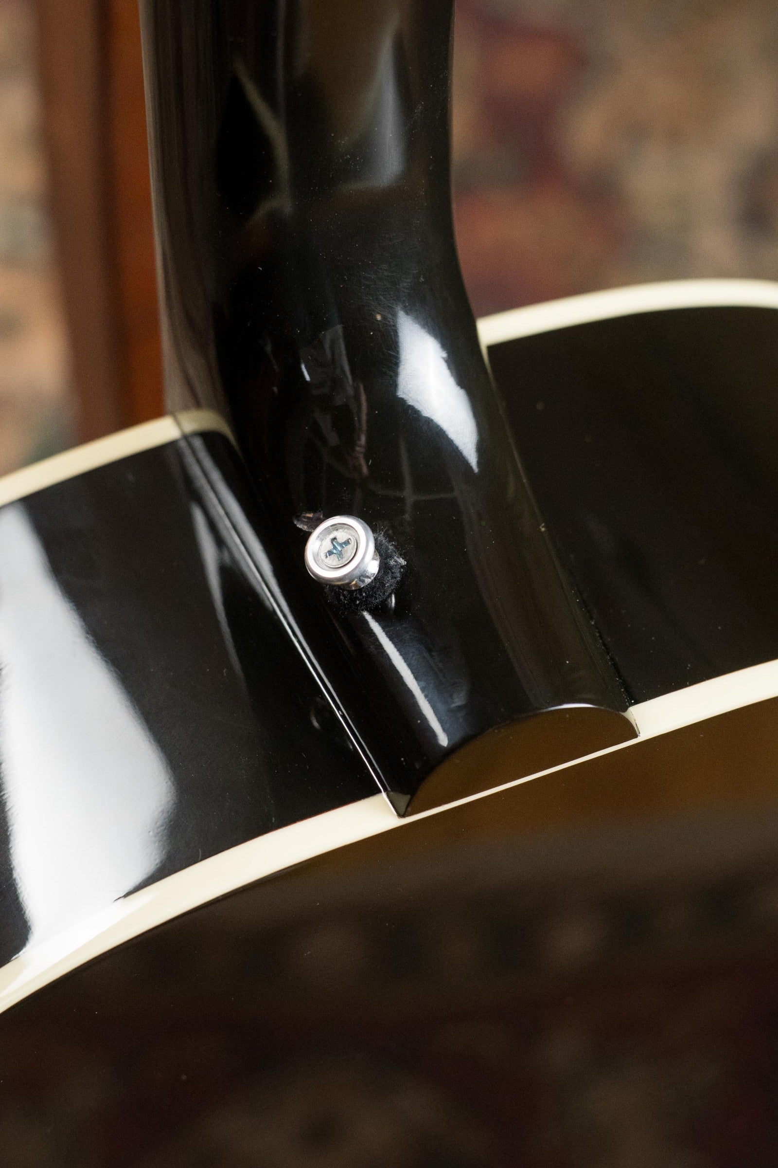 Close-up of the neck joint and strap button on this used Gibson J45 Standard Sitka/Mahogany Vintage Sunburst dreadnought (#4111) with cream binding, glossy finish, and K&K pickup; background is softly out of focus.
