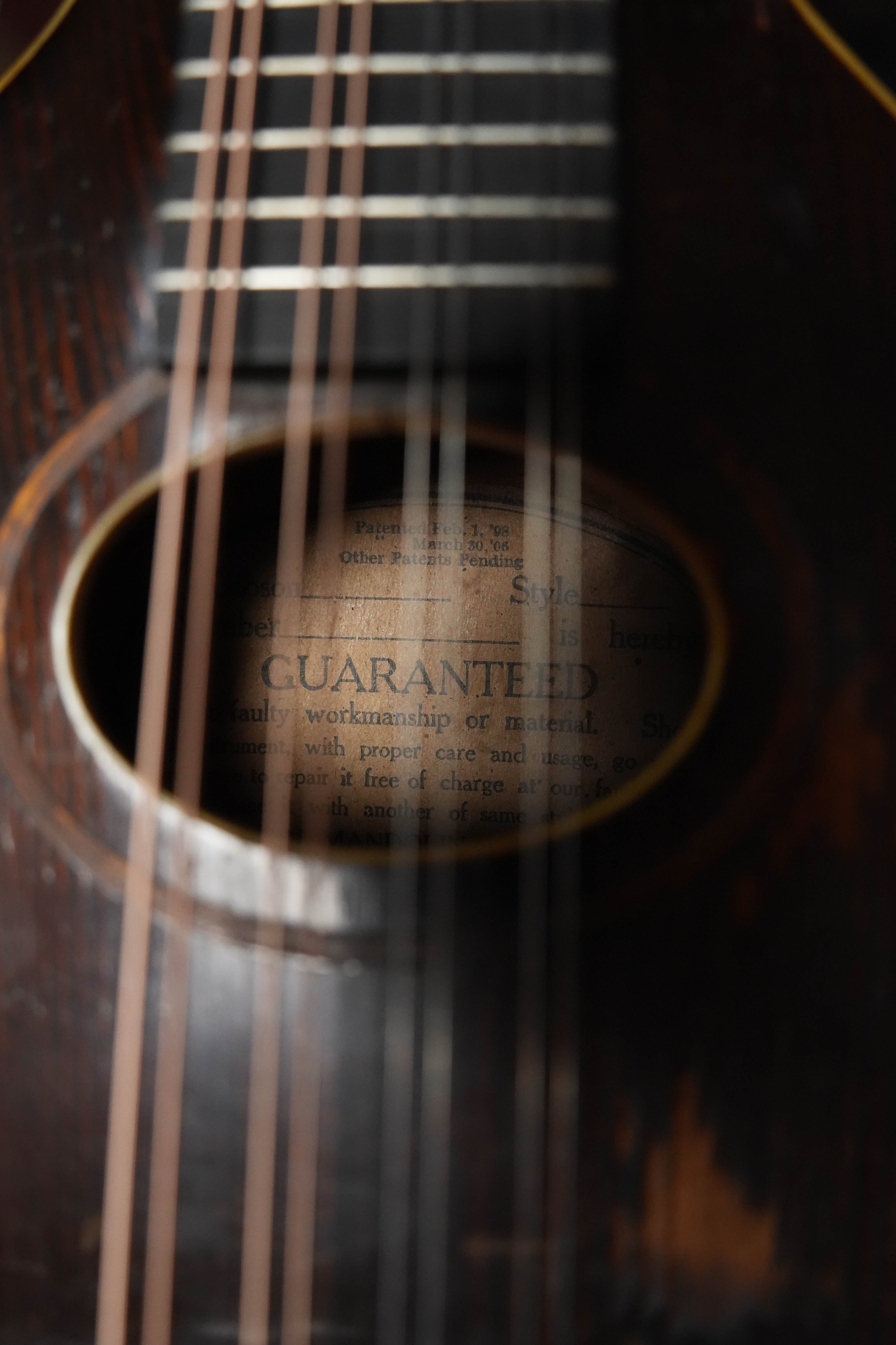 Close-up of a Gibson (Used) Vintage 1920 Spruce/Birch Oval-Hole Teardrop A-Style Mandolin #9066 sound hole, showing an old guarantee label inside the body, partially blurred by strings and the detailed wood grain.