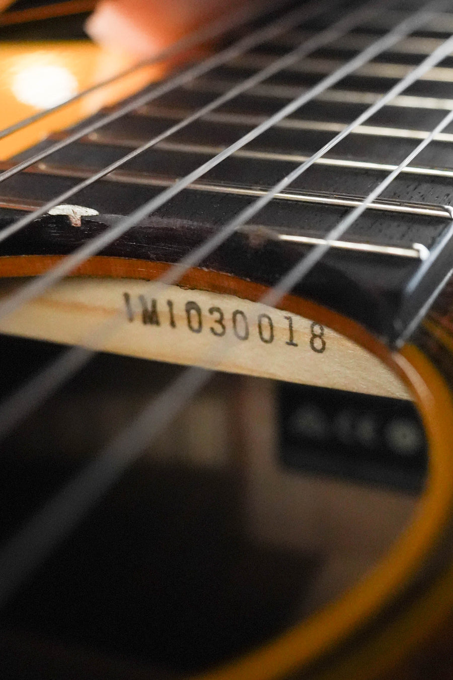 Close-up of a Yamaha CG-TA Spruce/Ovangkol TransAcoustic Nylon String Acoustic Guitar #0018’s sound hole and strings, with the serial number IM1030018 on the inside label. The solid spruce top and body are prominently featured in the foreground.