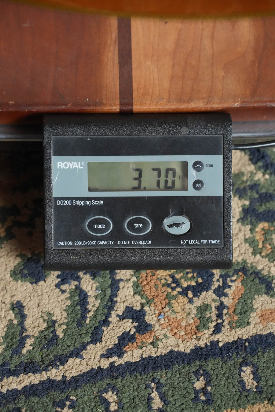 A Yamaha CG192C Cedar/Rosewood Classical Acoustic Guitar (#0188) by Yamaha rests on a digital shipping scale atop a patterned carpet, displaying a weight of 3.70 pounds.