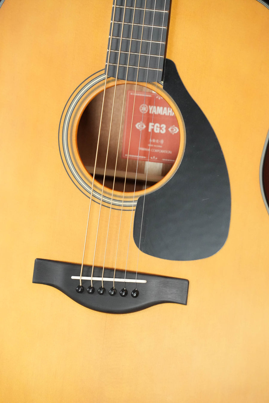 Close-up of the Yamaha FG3 Red Label Dreadnought Acoustic Guitar #1160, highlighting its strings, soundhole, pickguard, and bridge. Features a solid Sitka spruce top with a natural wood finish and Yamaha branding inside the soundhole.