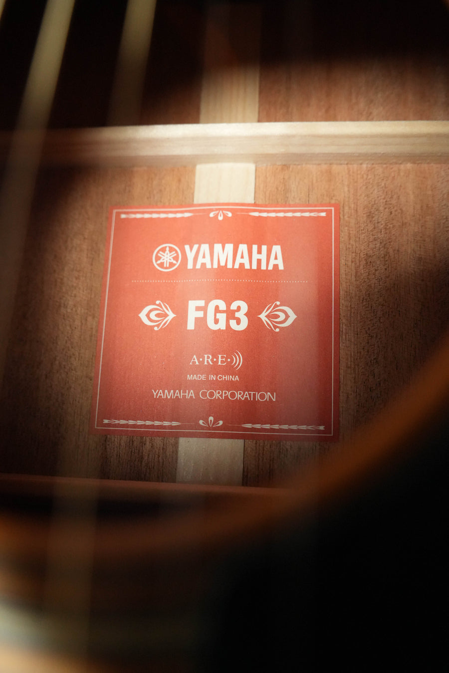 Close-up of a red inside label on the Yamaha FG3 Red Label Dreadnought Acoustic Guitar #1160, featuring A.R.E. technology and solid Sitka spruce top, made in China by Yamaha.