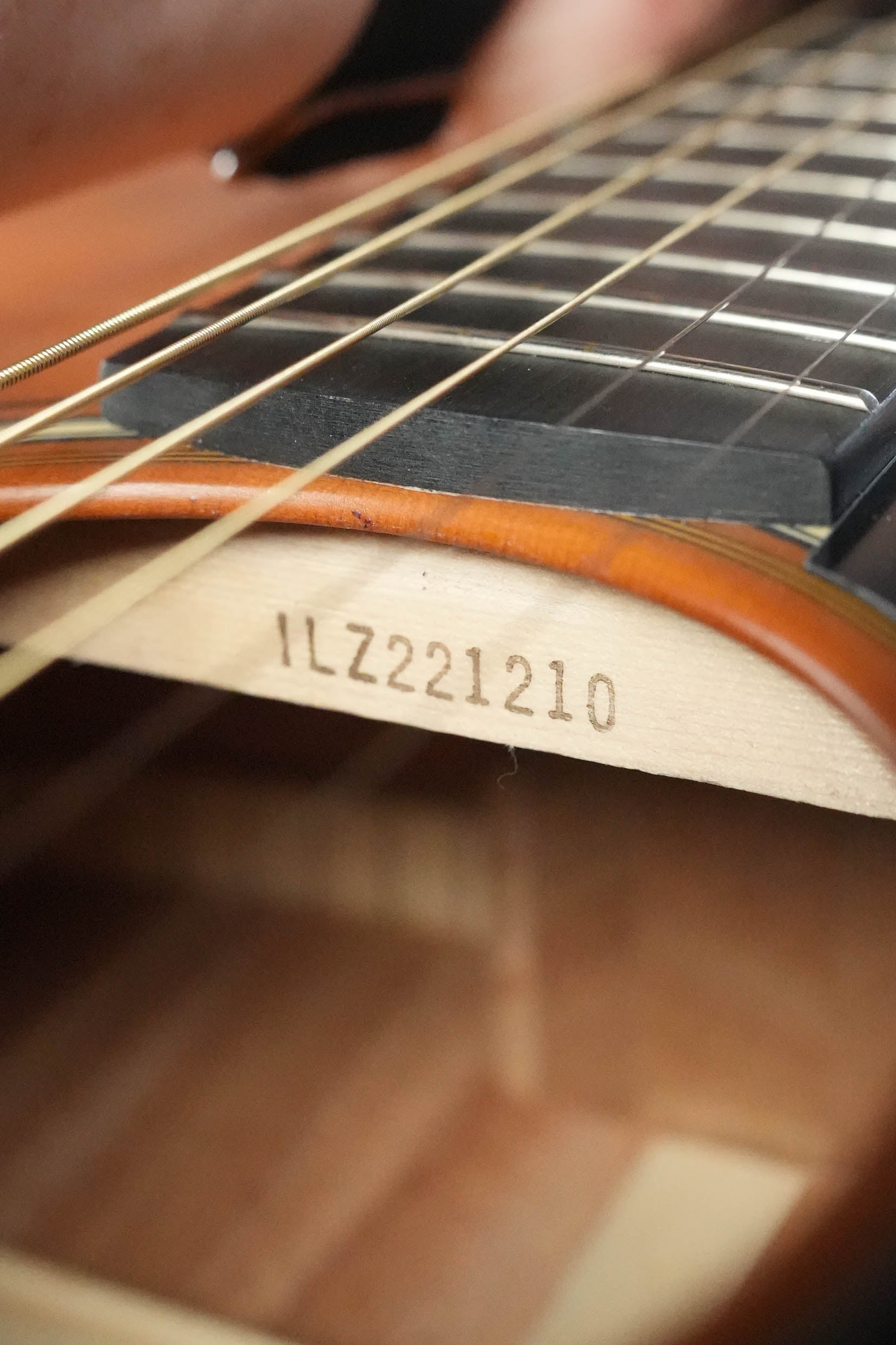 Close-up of the interior of a Yamaha FG3 Red Label Dreadnought Acoustic Guitar #1210, with the serial number ILZ221210 visible on the wood beneath the strings and fretboard.