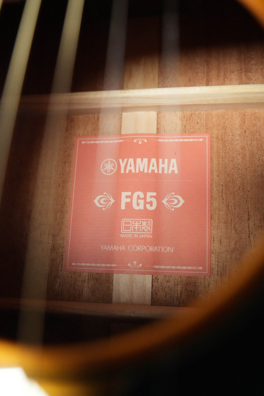 Close-up of a Yamaha FG5 GL NEW Gloss Red Label Dreadnought Acoustic Guitar #227A label inside the instrument, showing "Yamaha FG5 Made in Japan Yamaha Corporation" on a red background, framed by strings and Sitka spruce top.
