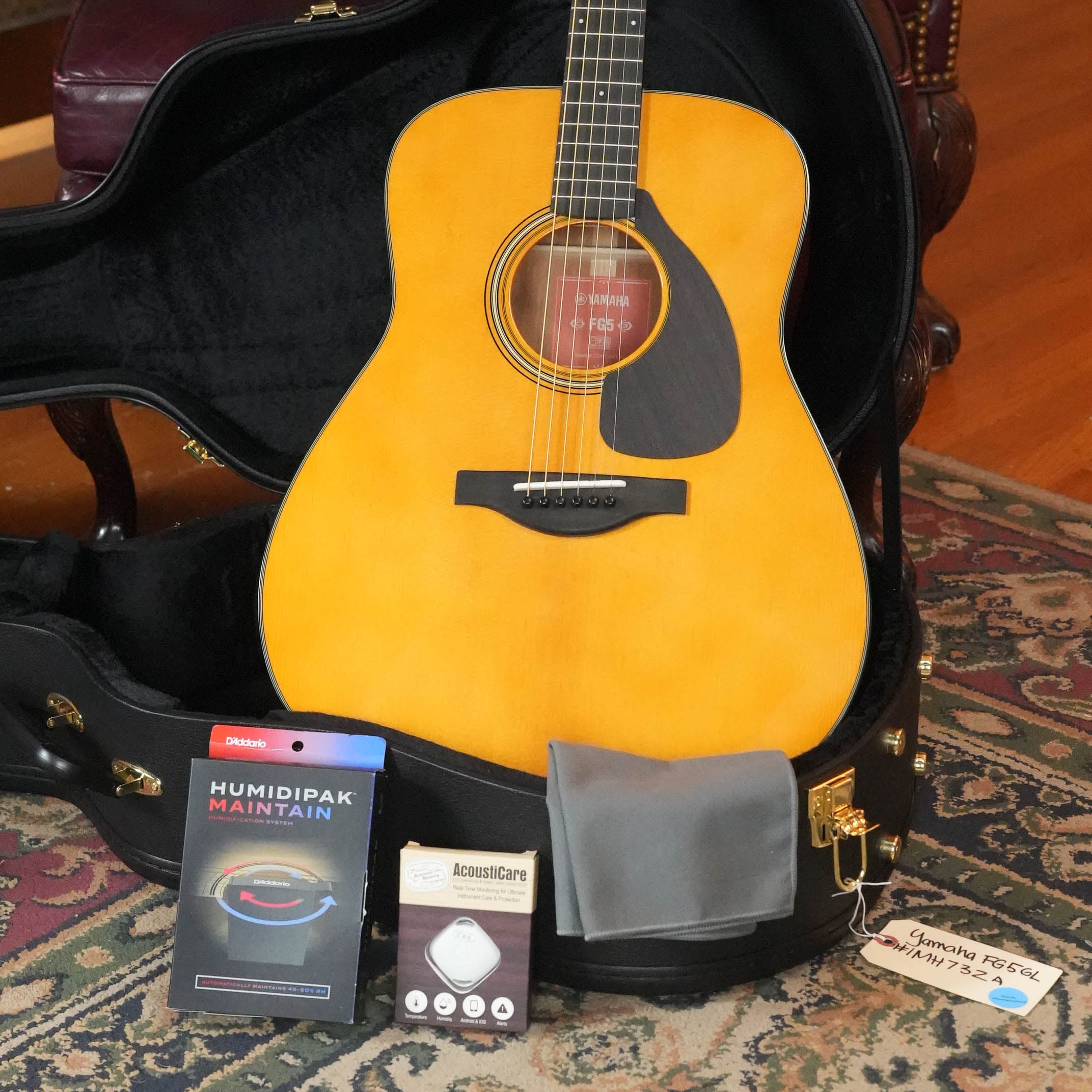The Yamaha FG5 GL NEW Gloss Red Label Dreadnought Acoustic Guitar #732A, featuring a solid Sitka spruce top, rests in an open hard case with a gray cloth, two care packages, and a handwritten note on the rug.