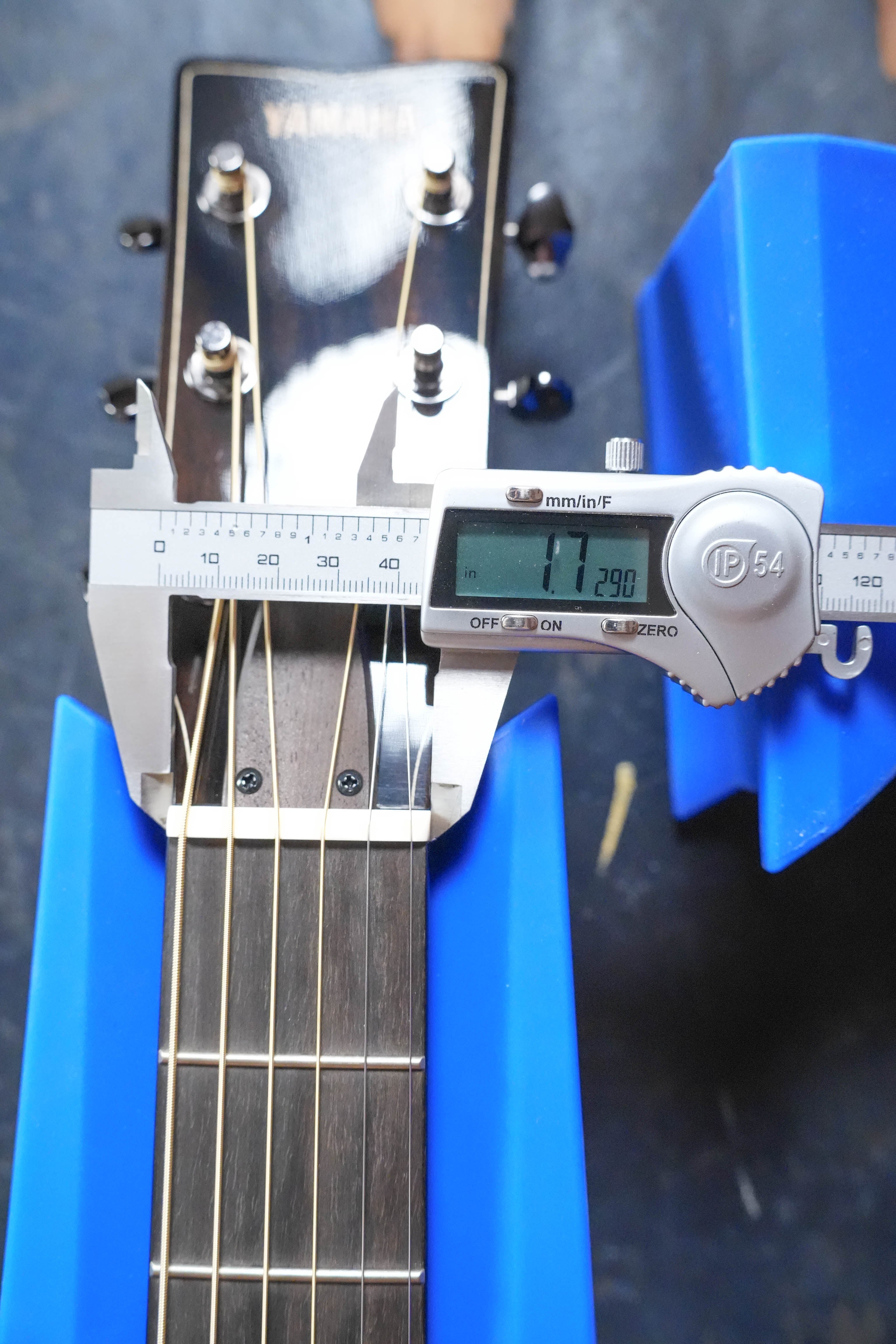 A digital caliper measures the nut width of the Yamaha FG9 M Adirondack/Mahogany Dreadnought Acoustic Guitar #112A, displaying 42.90 mm, with the Yamaha logo headstock resting on blue supports.