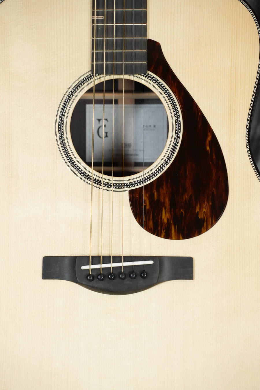 Close-up of a Yamaha FG9 R NT Adirondack/Indian Rosewood Dreadnought Acoustic Guitar #113A, showing its sound hole, strings, bridge, and tortoiseshell-patterned pickguard with a window reflected on the glossy spruce top.