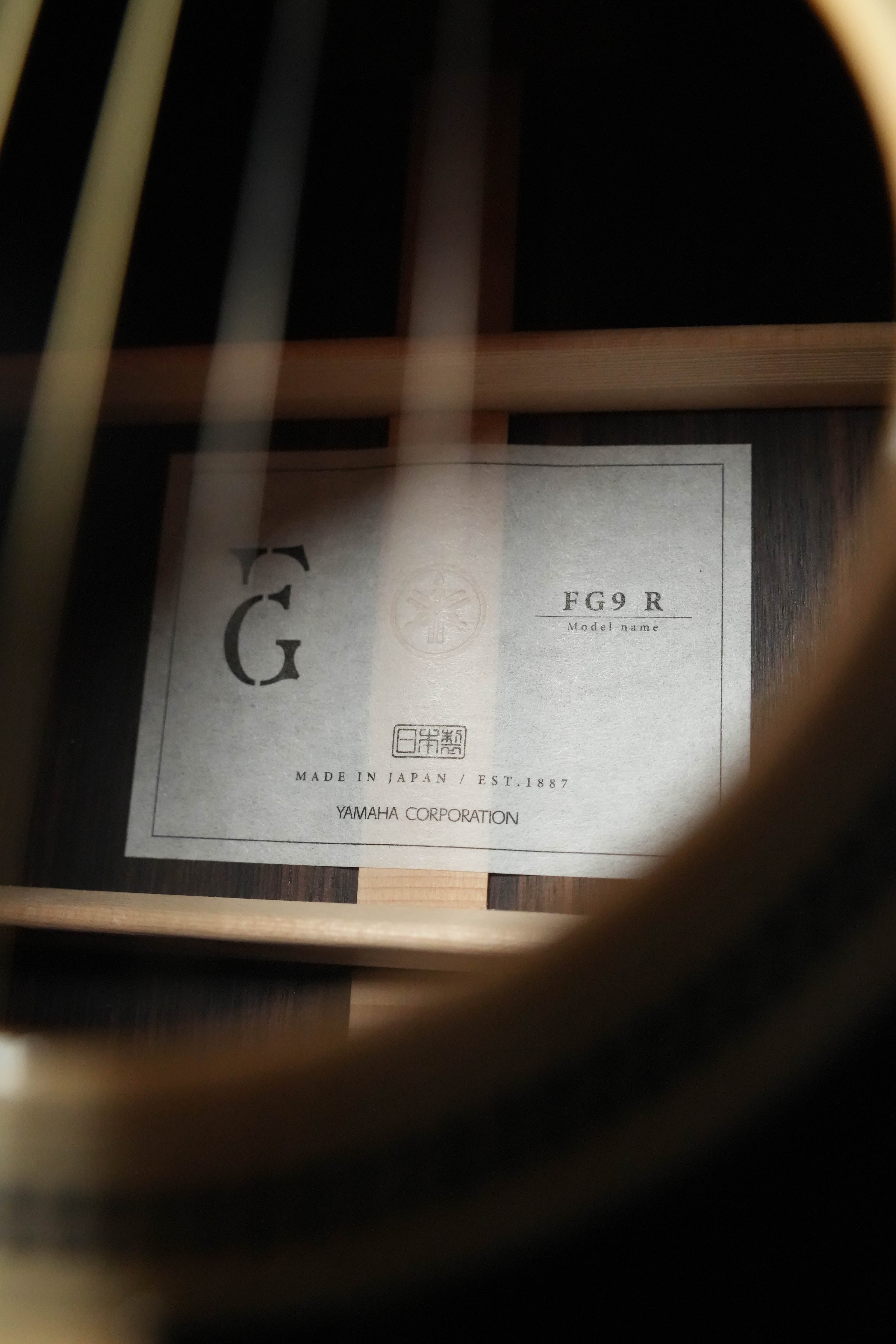 A close-up through the guitar strings reveals a label inside the Yamaha FG9 R NT Natural Finish Dreadnought Acoustic Guitar #126A, marked “Yamaha,” “Made in Japan,” and showcasing its Adirondack spruce craftsmanship.